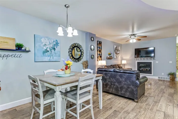 Open-concept interior featuring wood-finish flooring, a contemporary fireplace with a white mantel, and a ceiling fan with integrated lighting