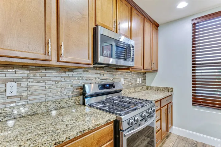 Kitchen featuring wood-finish cabinetry, granite countertops, and a full-height mosaic tile backsplash