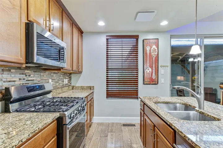 Kitchen featuring wood-finish cabinetry, stainless steel appliances, granite countertops, and a tile backsplash