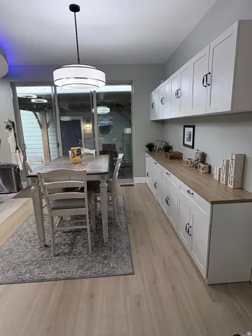 Open concept area featuring light wood-finish flooring, white shaker-style cabinetry with matte black hardware, and a wood-finish countertop