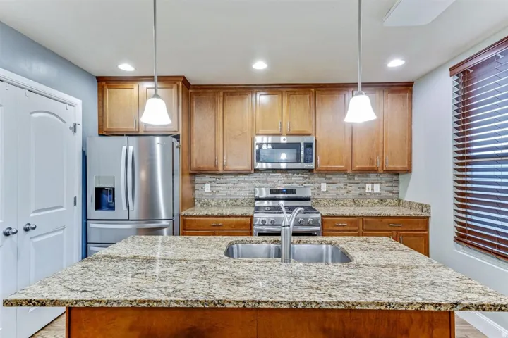 Kitchen featuring a large island with an undermount double basin stainless steel sink, granite countertops, wood cabinetry, and stainless steel appliances