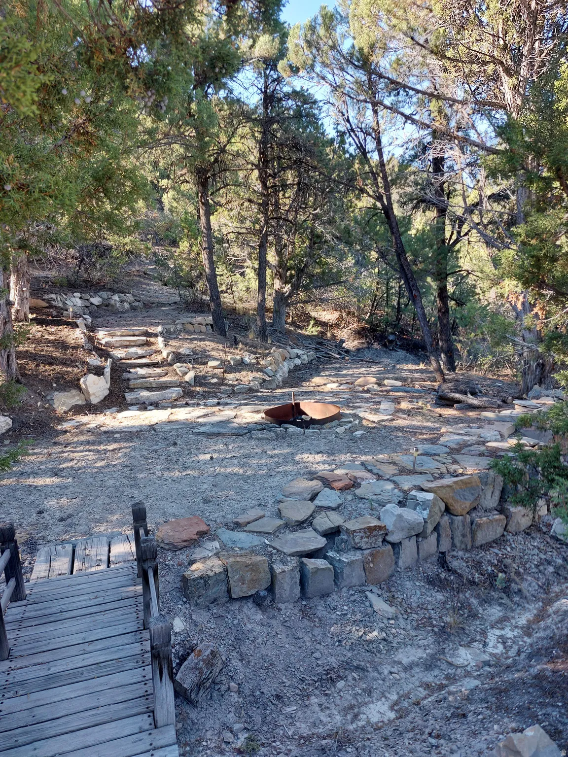 Terraced outdoor space featuring stone steps, a natural wood walkway, and mature trees creating a shaded environment