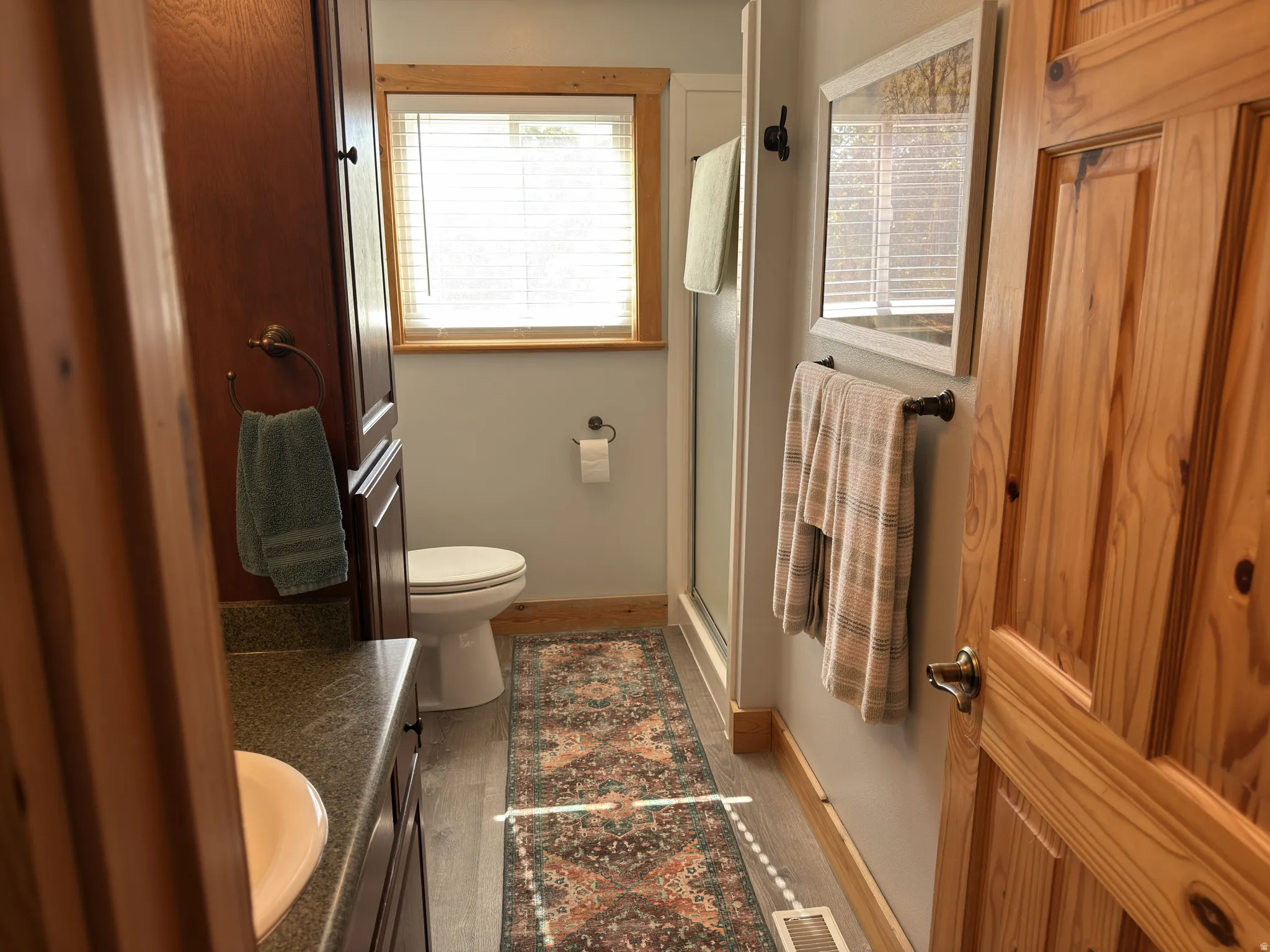 Bathroom featuring a wood-finish vanity with an integrated sink, a commode, a shower enclosure, and laminate flooring