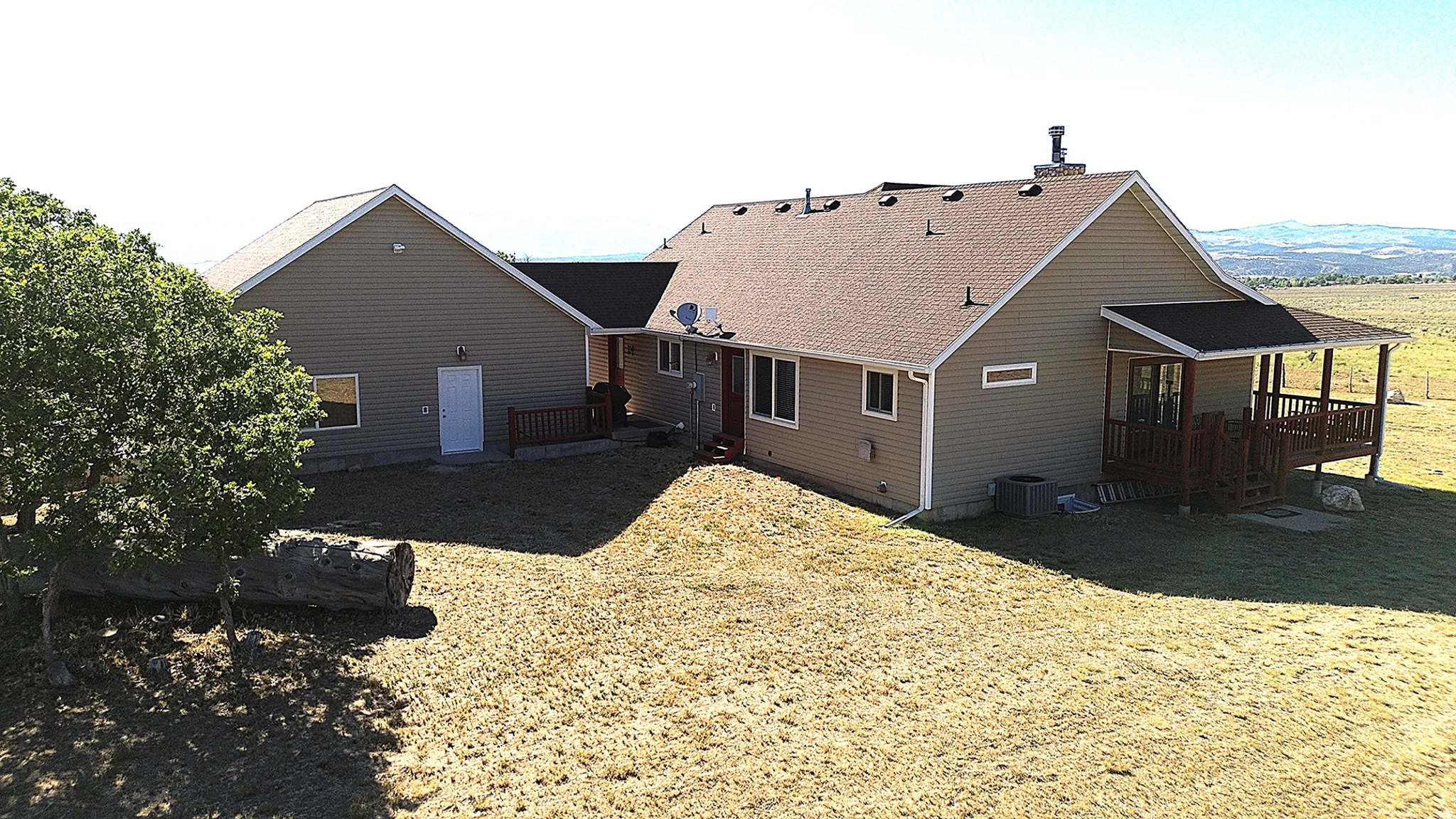 Expansive backyard with a covered wooden porch, light brown siding, and a brown shingle roof