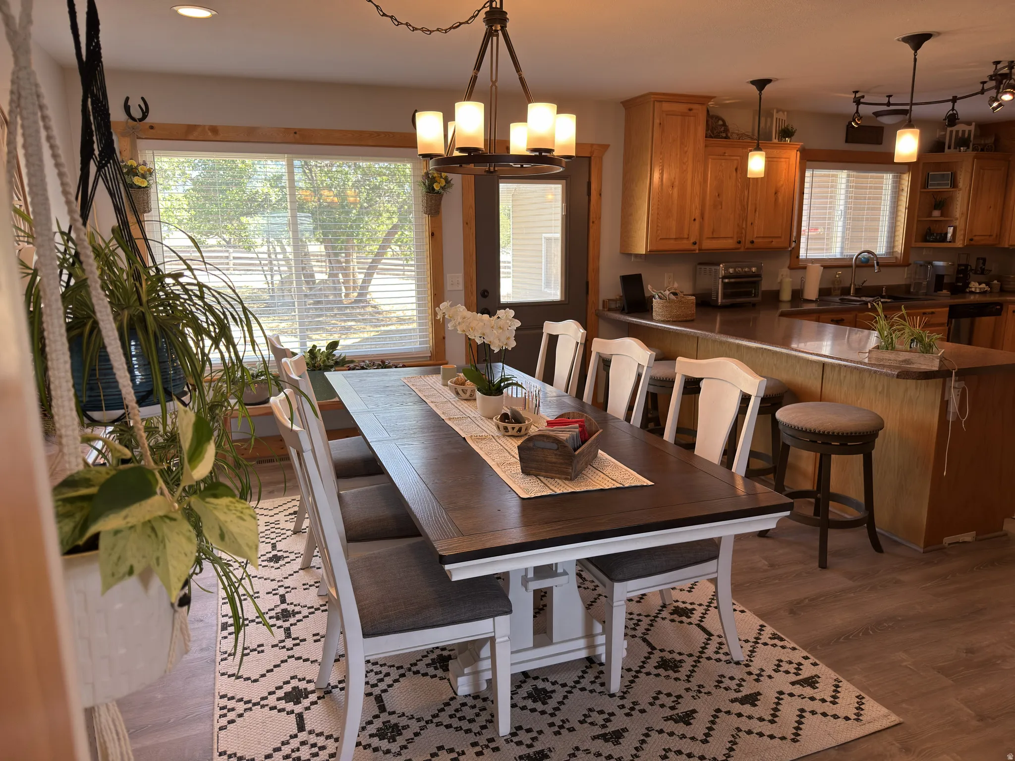 Open-concept dining area featuring laminate flooring, a contemporary chandelier, and a large window with natural wood trim and exterior door to the yard.