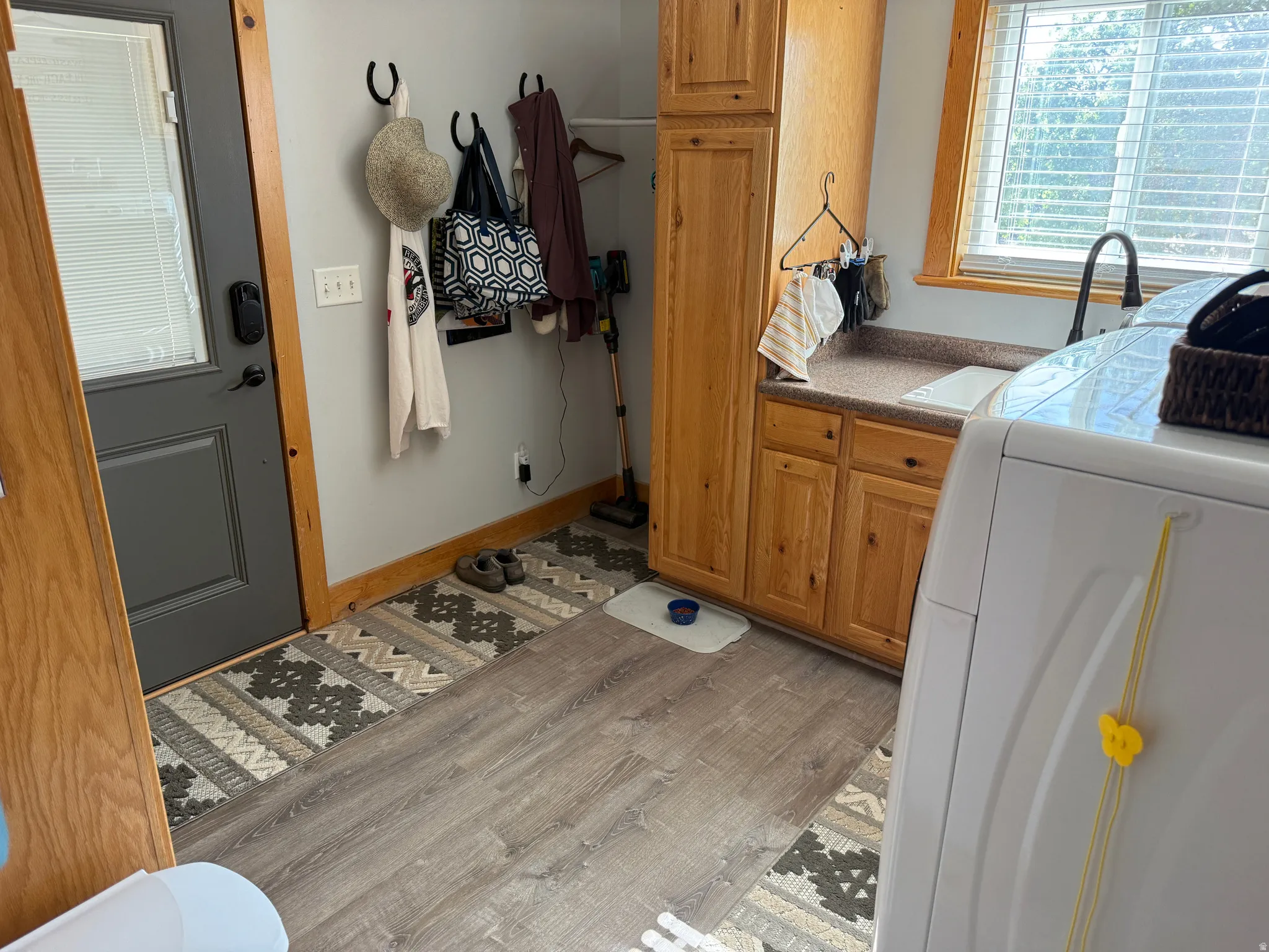 Utility room featuring recently installed laminate flooring, natural wood cabinetry, and a countertop with an integrated sink