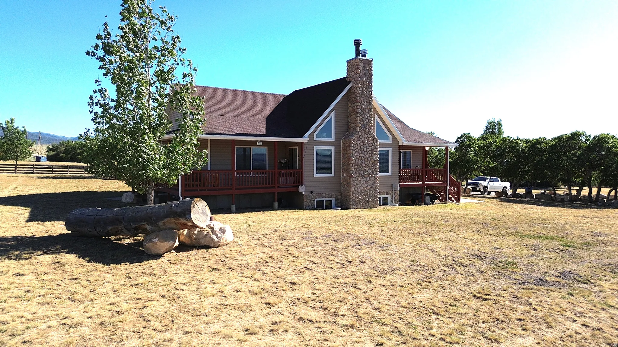 Exterior featuring a stone chimney, multiple large windows, and a covered deck