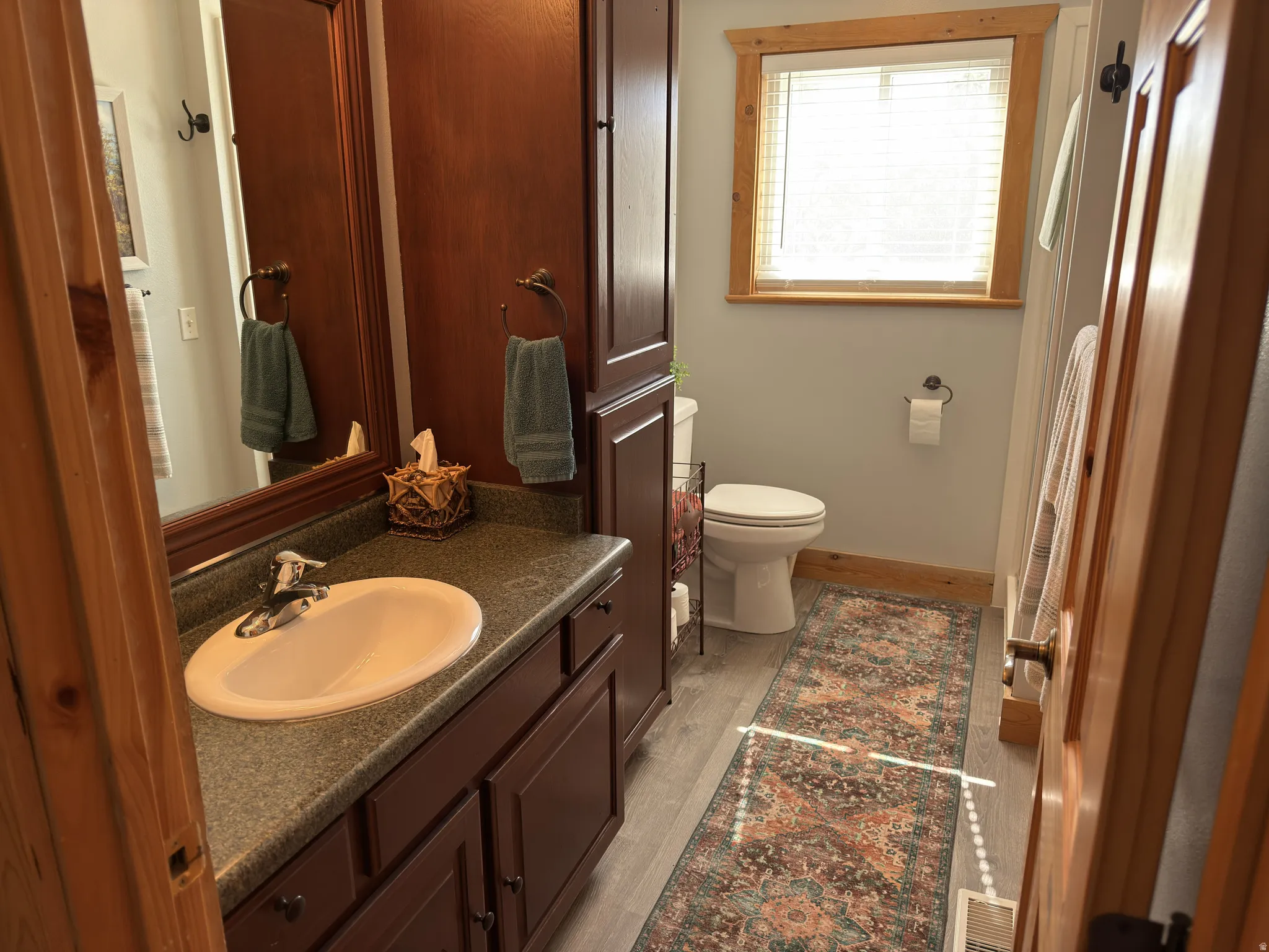 Bathroom featuring a wood-finish vanity with an integrated sink and dark countertop, framed wall mirror, and built-in storage cabinetry