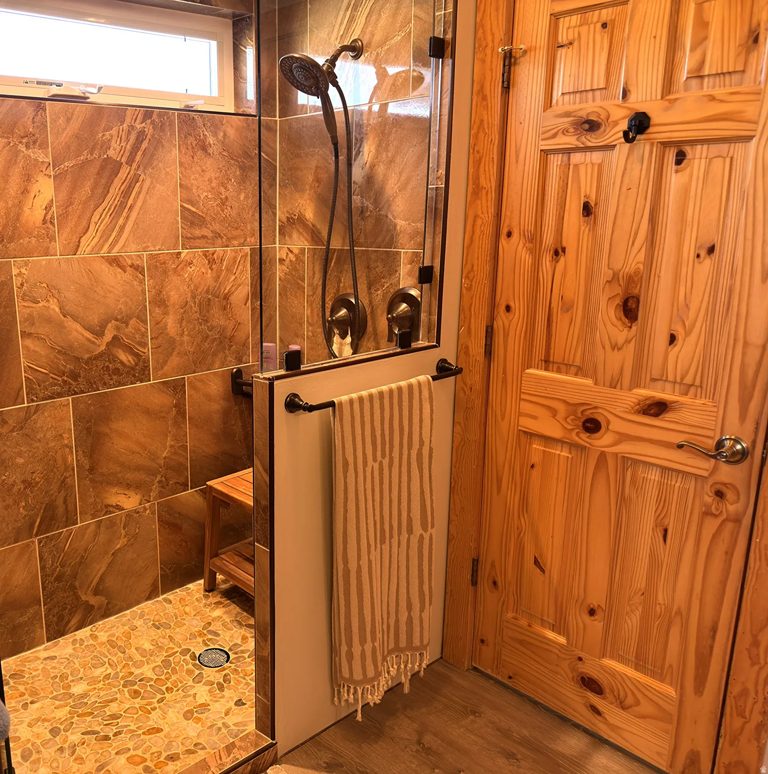 Walk-in shower with natural stone tile walls and pebble floor and window.