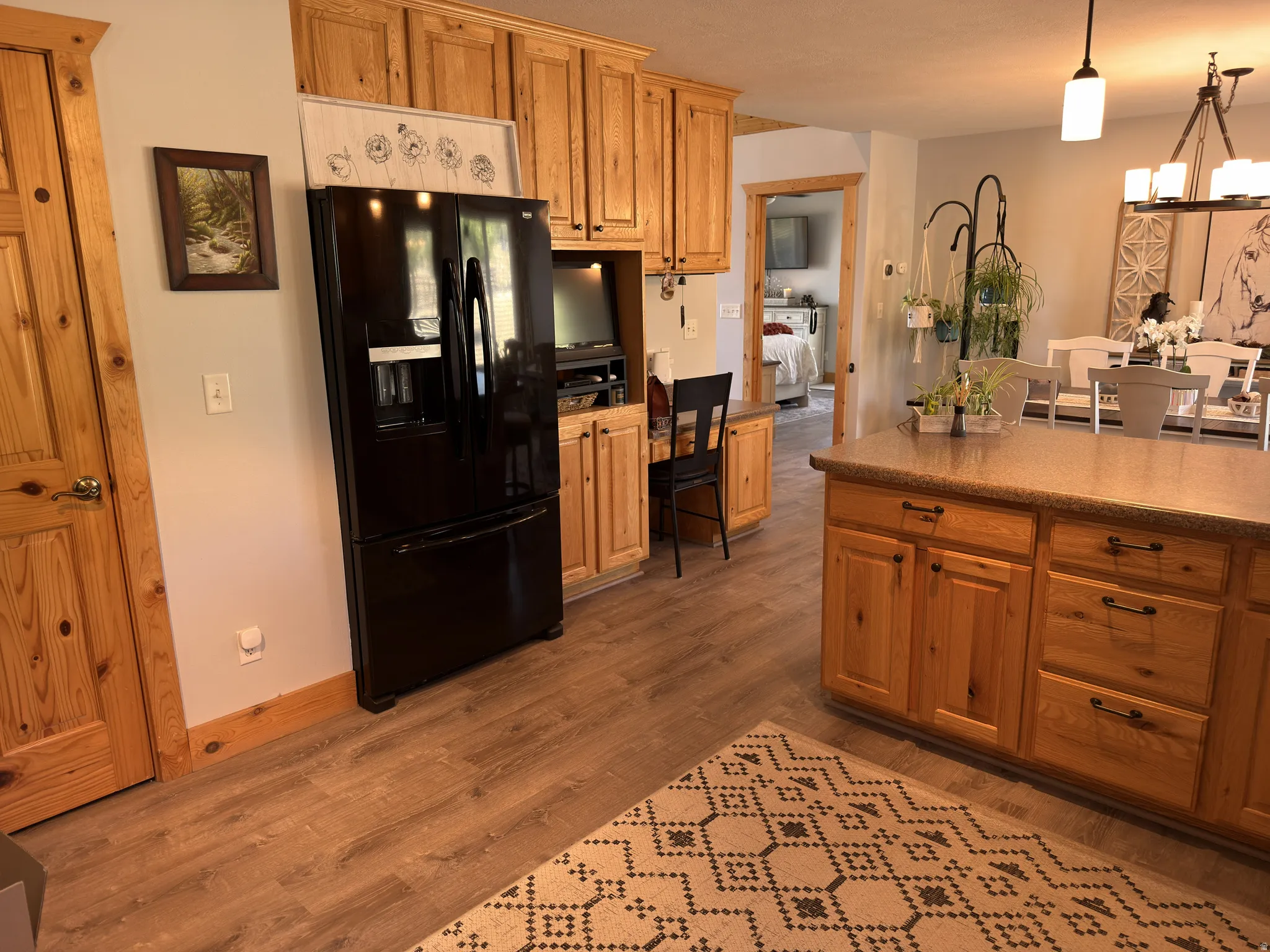 Kitchen featuring laminate flooring, natural wood cabinetry, a built-in desk area, a peninsula bar with integrated storage, and an open concept to the dining area