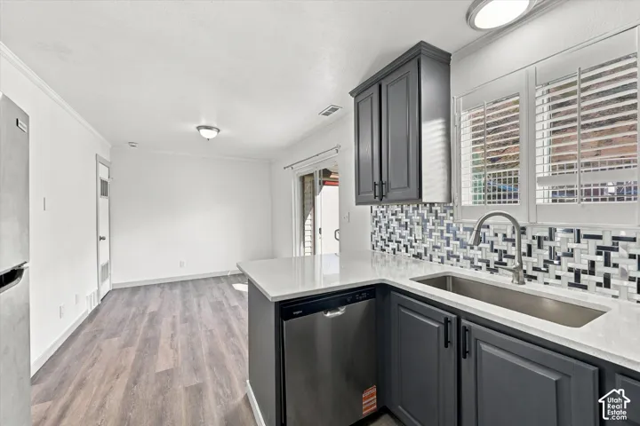Kitchen featuring dark gray cabinetry, stainless steel appliances, a mosaic tile backsplash, white countertops, and wood-finish flooring