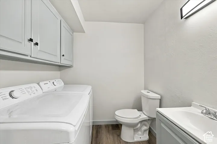 Half Bath at main floor with a Laundry. Built-in cabinetry, wood-finish flooring, wall-mounted light fixture, white toilet, and vanity with integrated sink