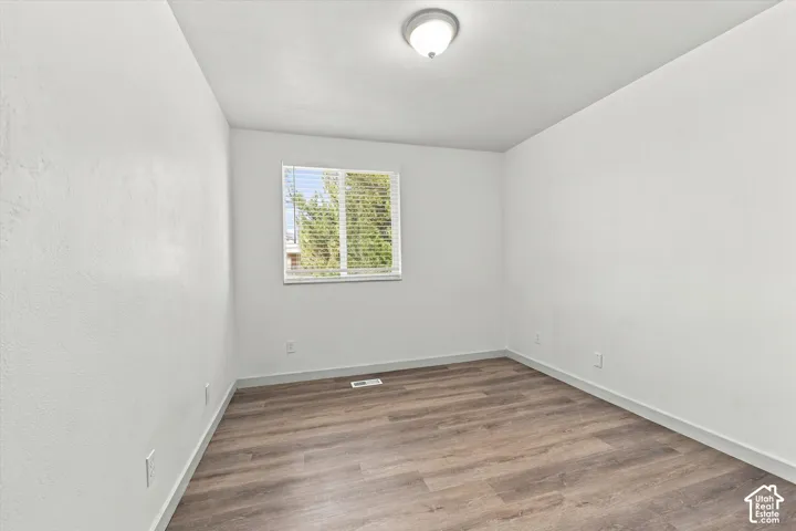 Bedroom #2. Wood-finish flooring with white walls and a single window featuring blinds