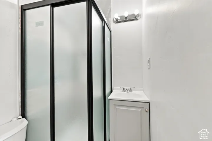 Frosted glass shower enclosure with black framing, single vanity with integrated sink, and modern three-bulb fixture