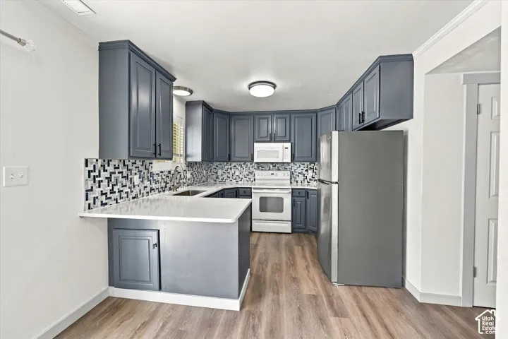 Kitchen featuring abundant gray cabinetry, white countertops, mosaic tile backsplash, wood-finish flooring, and a stainless steel refrigerator