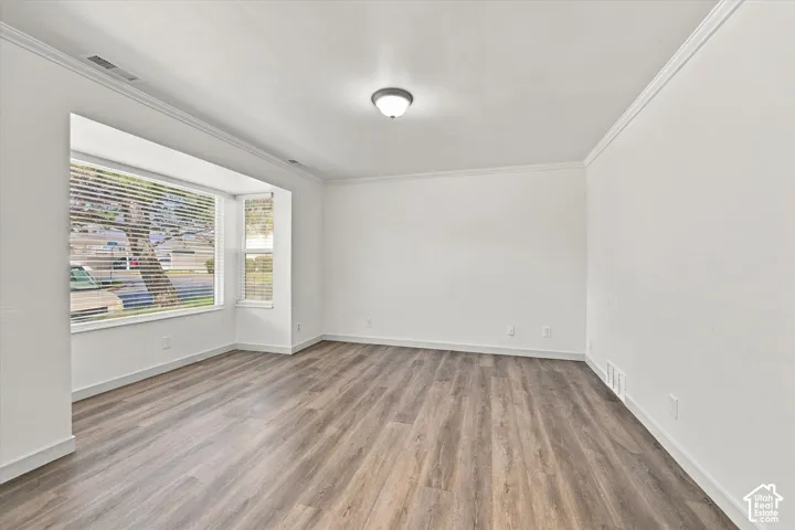 Spacious room featuring a bay window, wood-finish flooring, crown molding, and recessed lighting