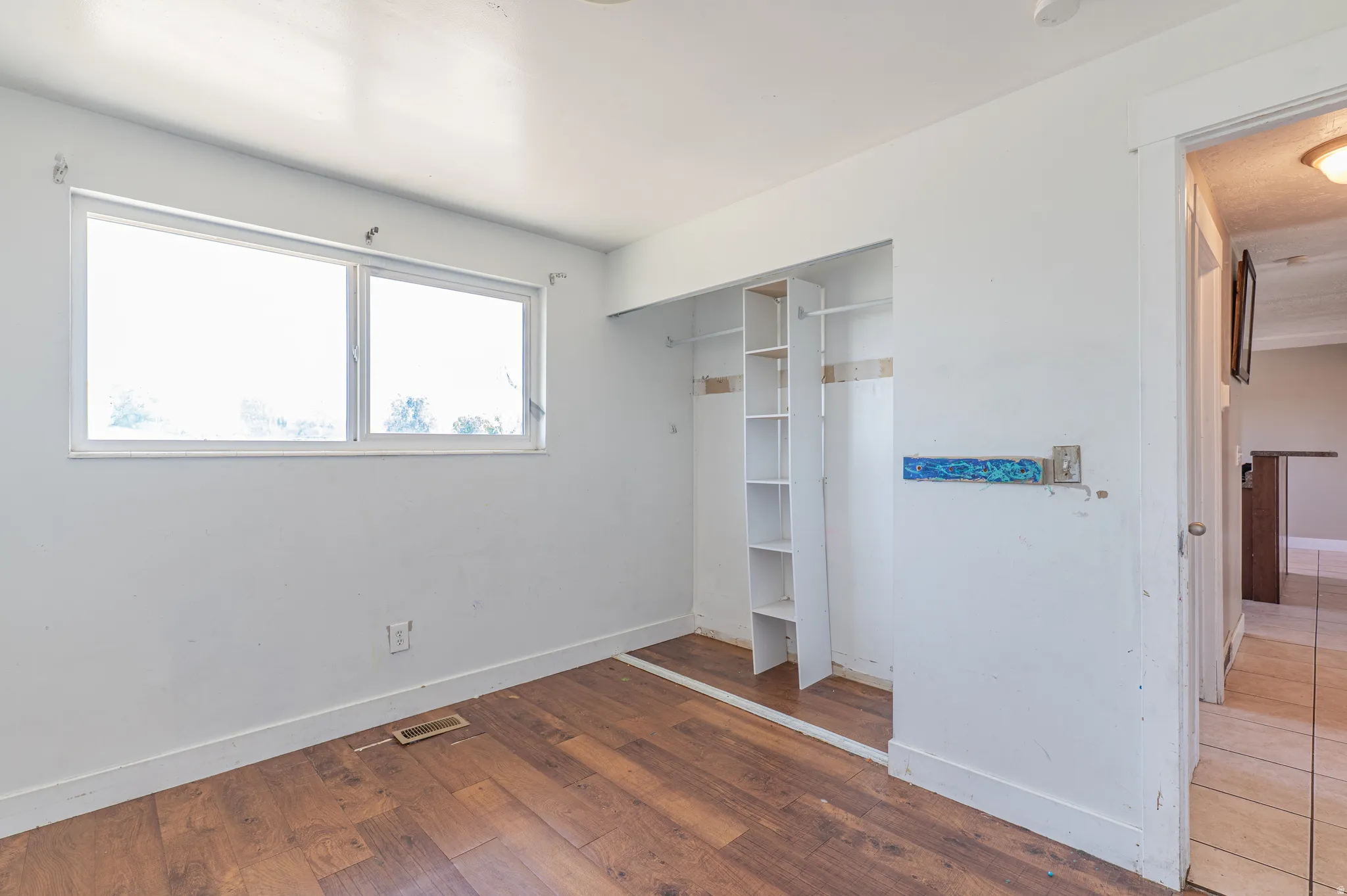 Room featuring wood-finish flooring, a large window, a built-in closet with shelving, white baseboards, and neutral wall finishes