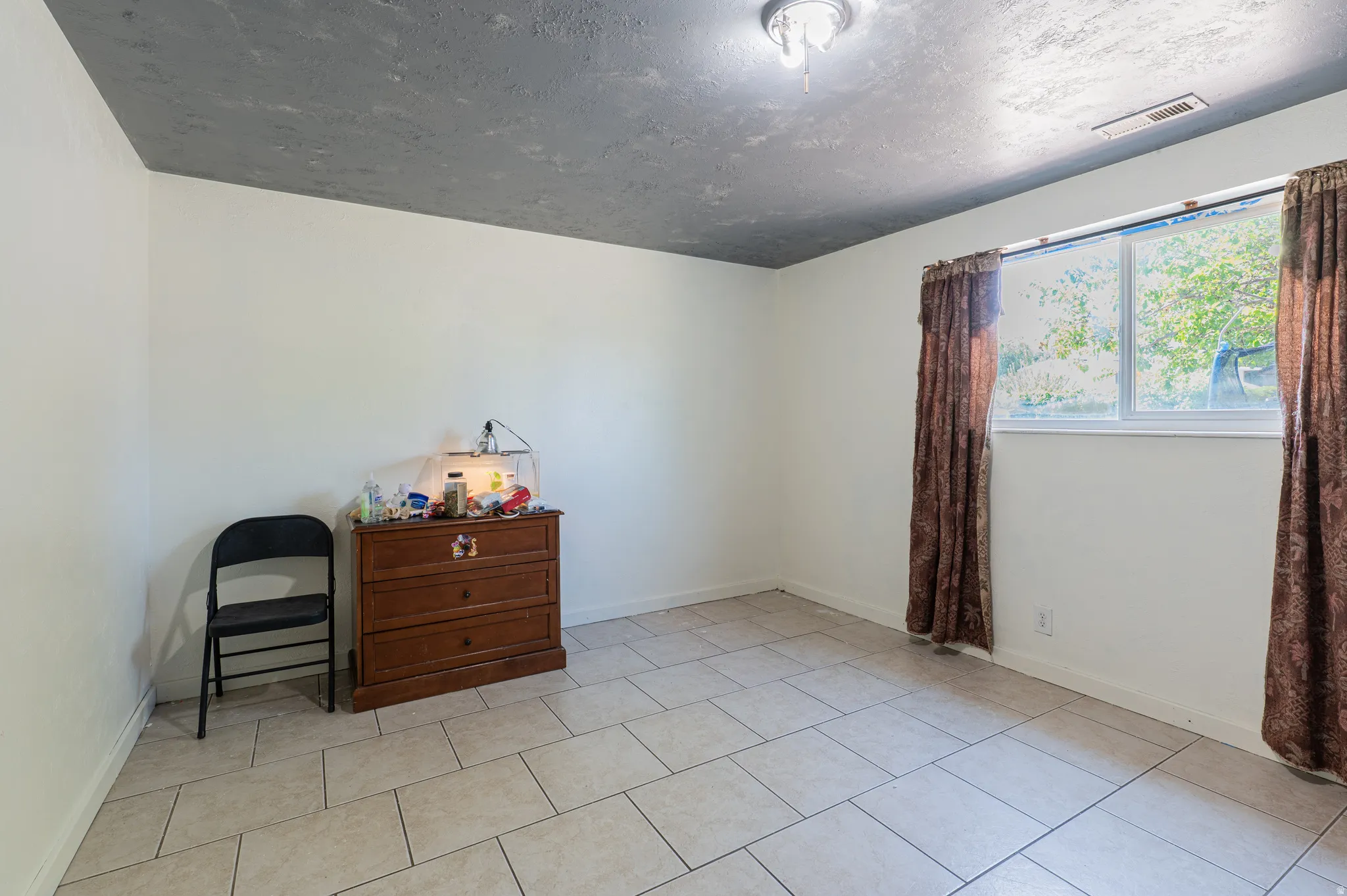 Room featuring light-colored tile flooring, white walls, and a textured gray ceiling