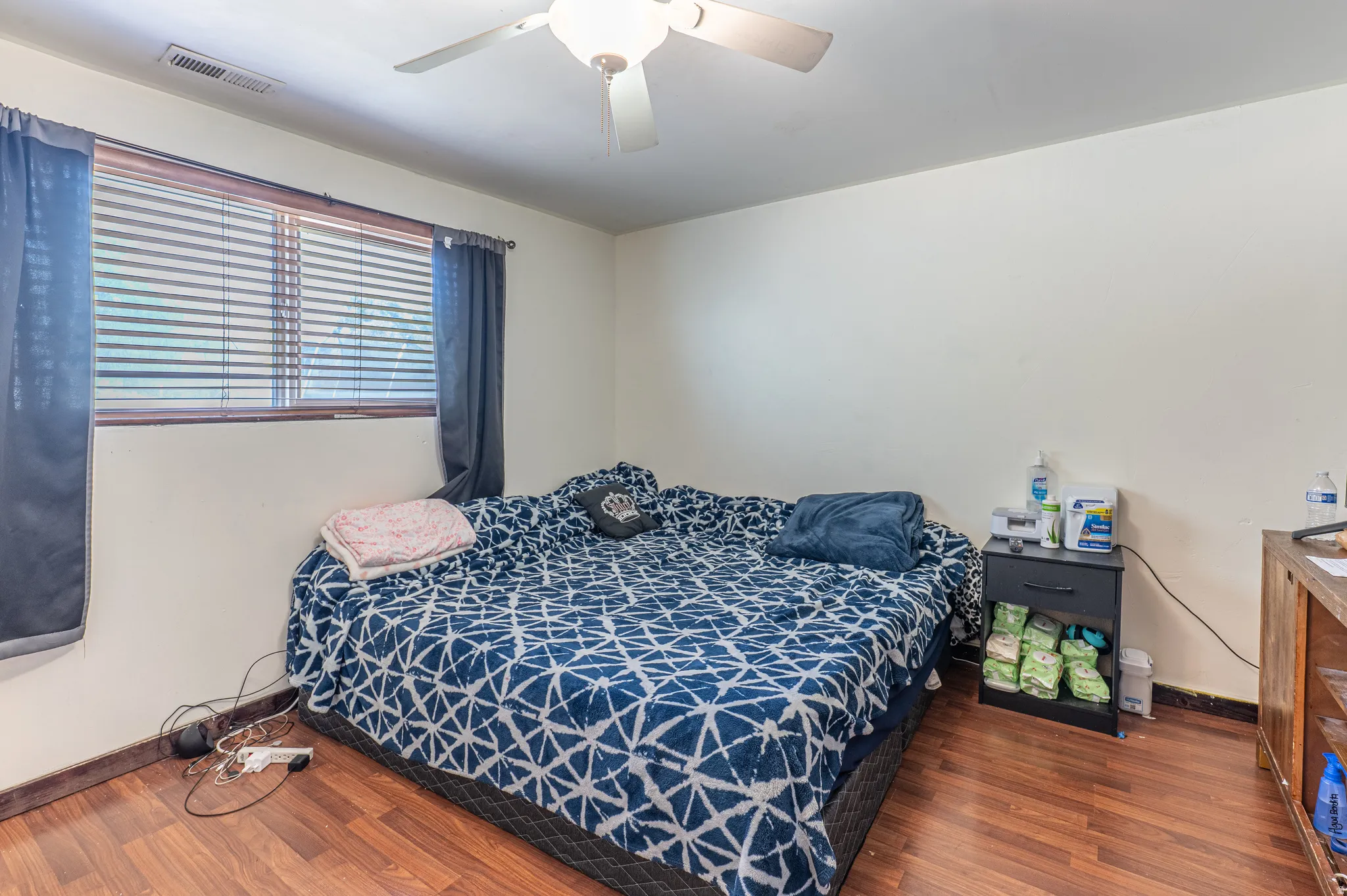 Bright room featuring wood-finish flooring, a window with horizontal blinds, and a ceiling fan with integrated lighting