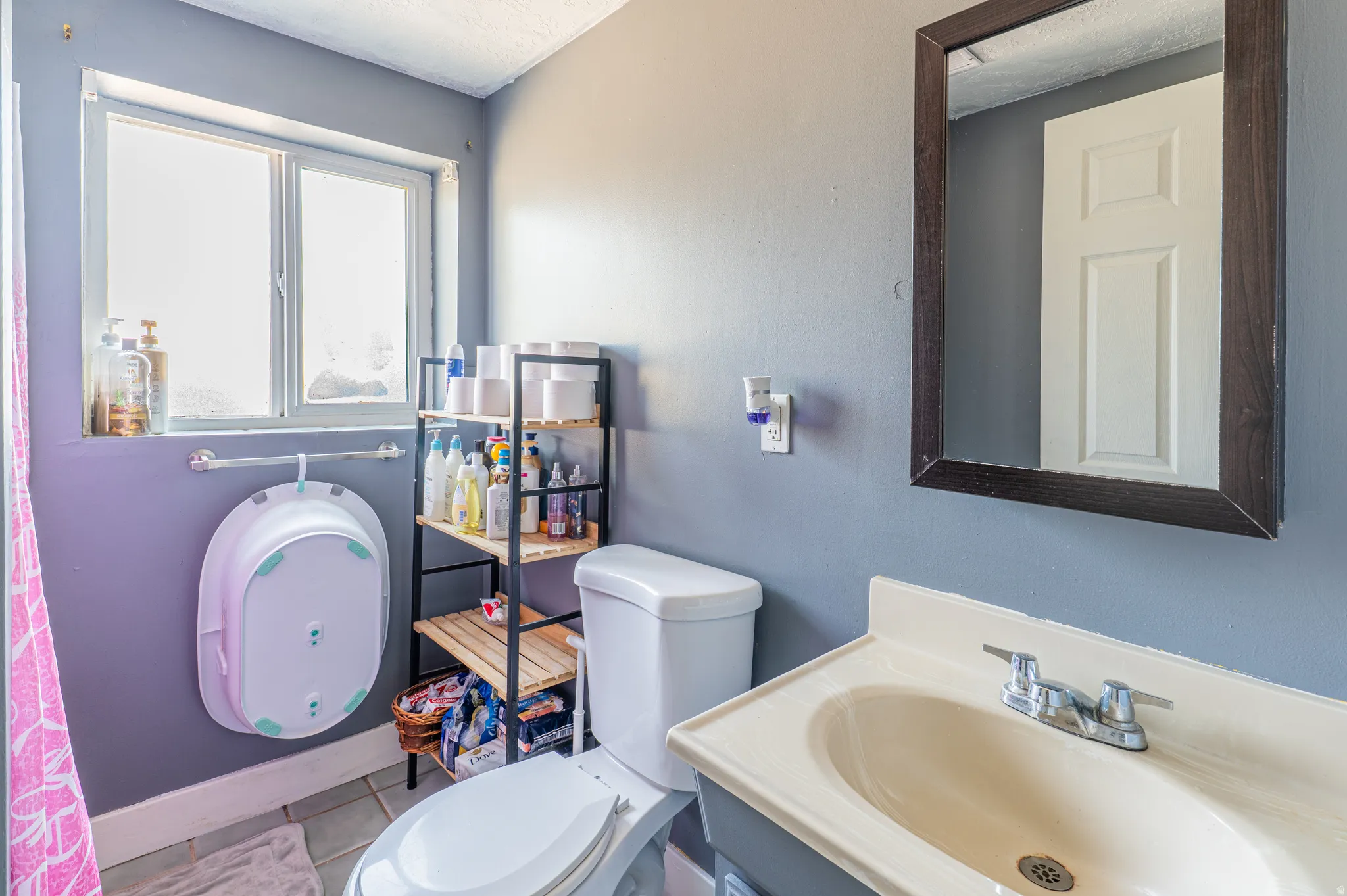 Bathroom featuring a single window, a wall-mounted mirror with a dark frame, a toilet, and a vanity with an integrated sink and chrome faucet