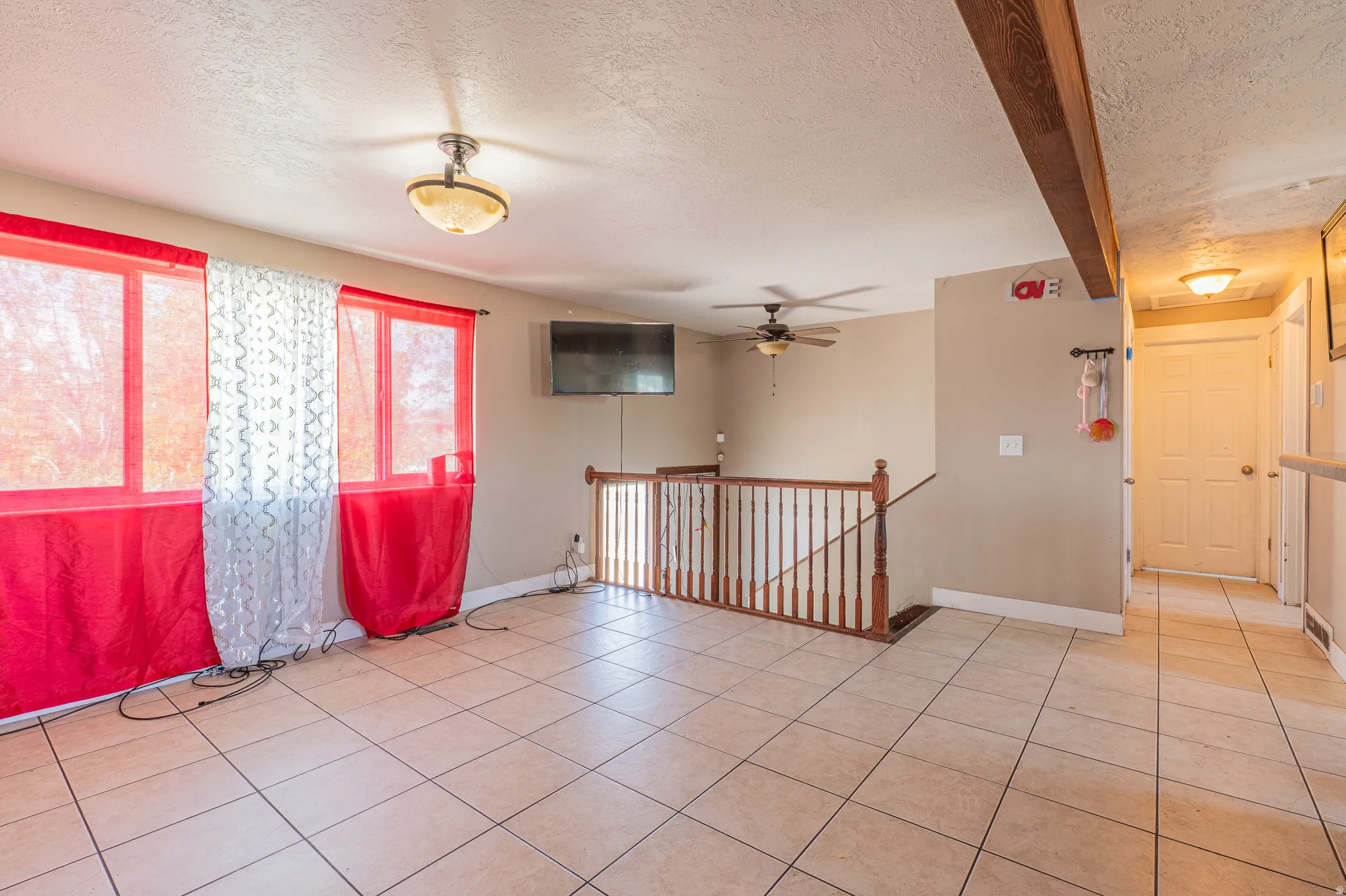 Spacious interior room featuring light-toned tile flooring, multiple windows providing natural illumination, and a wooden baluster railing