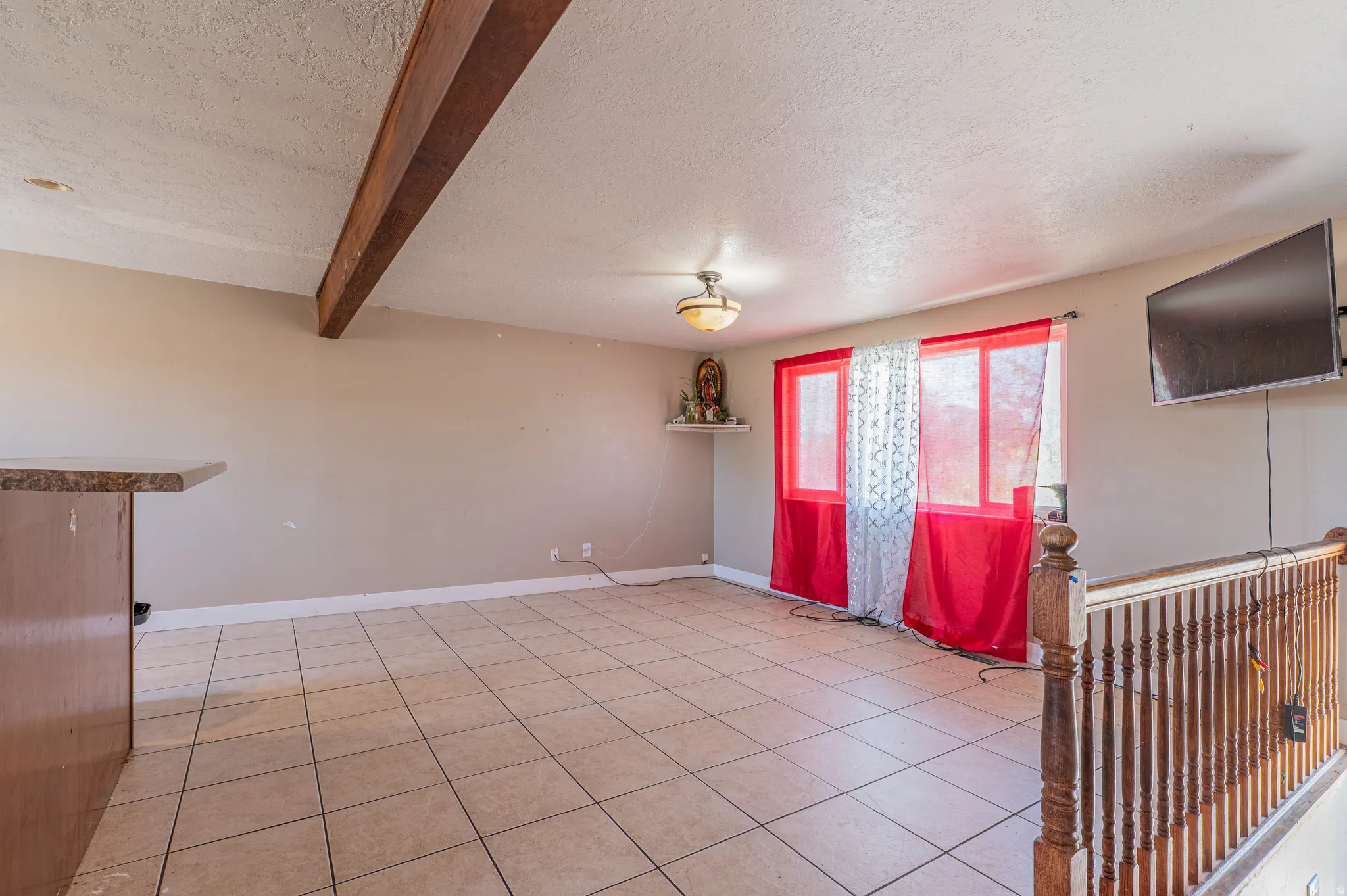 Spacious room featuring tile flooring, a wood ceiling beam, and a built-in breakfast bar with a stone-finish countertop