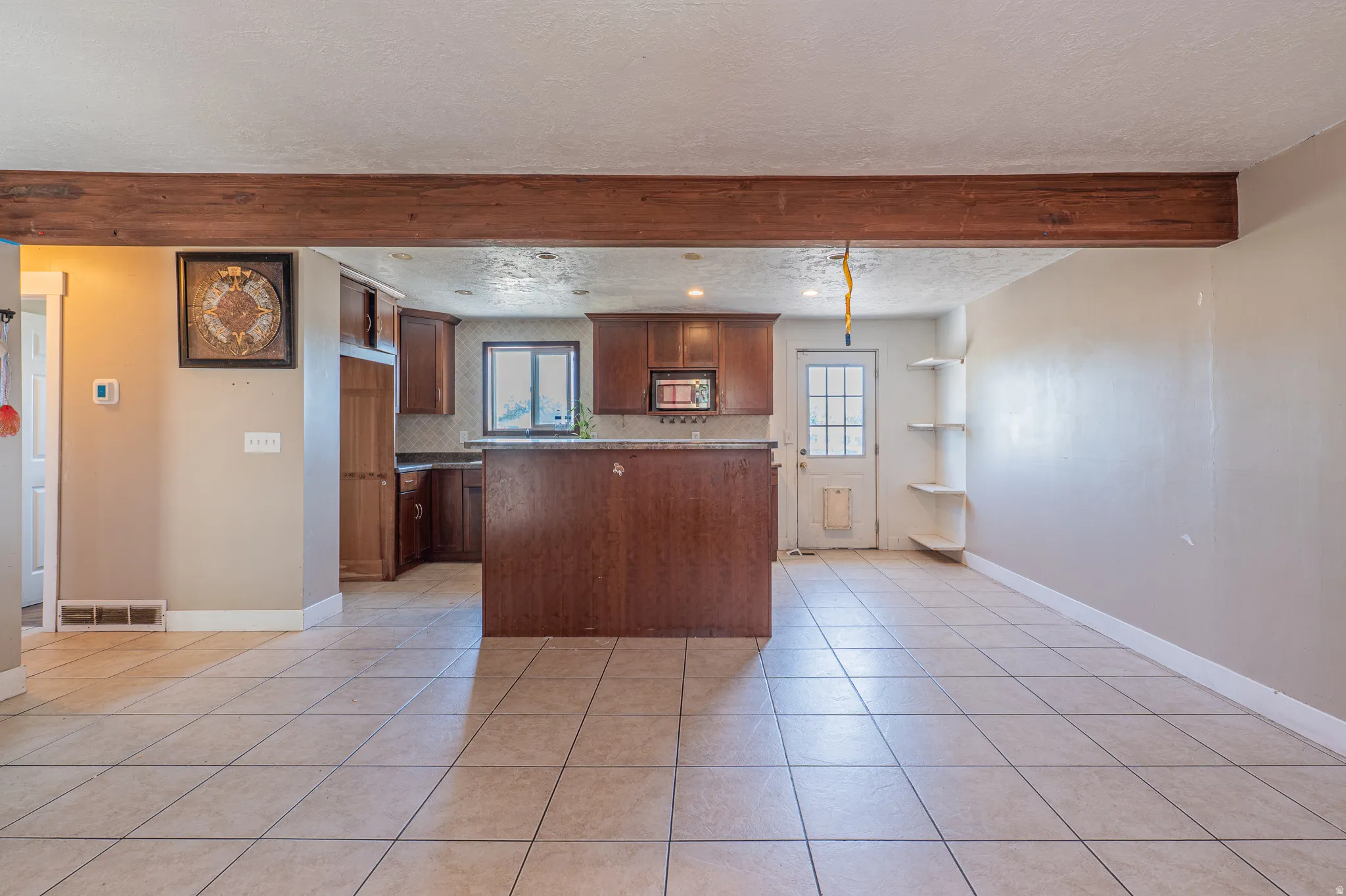 Open-concept living space with large format tile flooring and an exposed wood beam