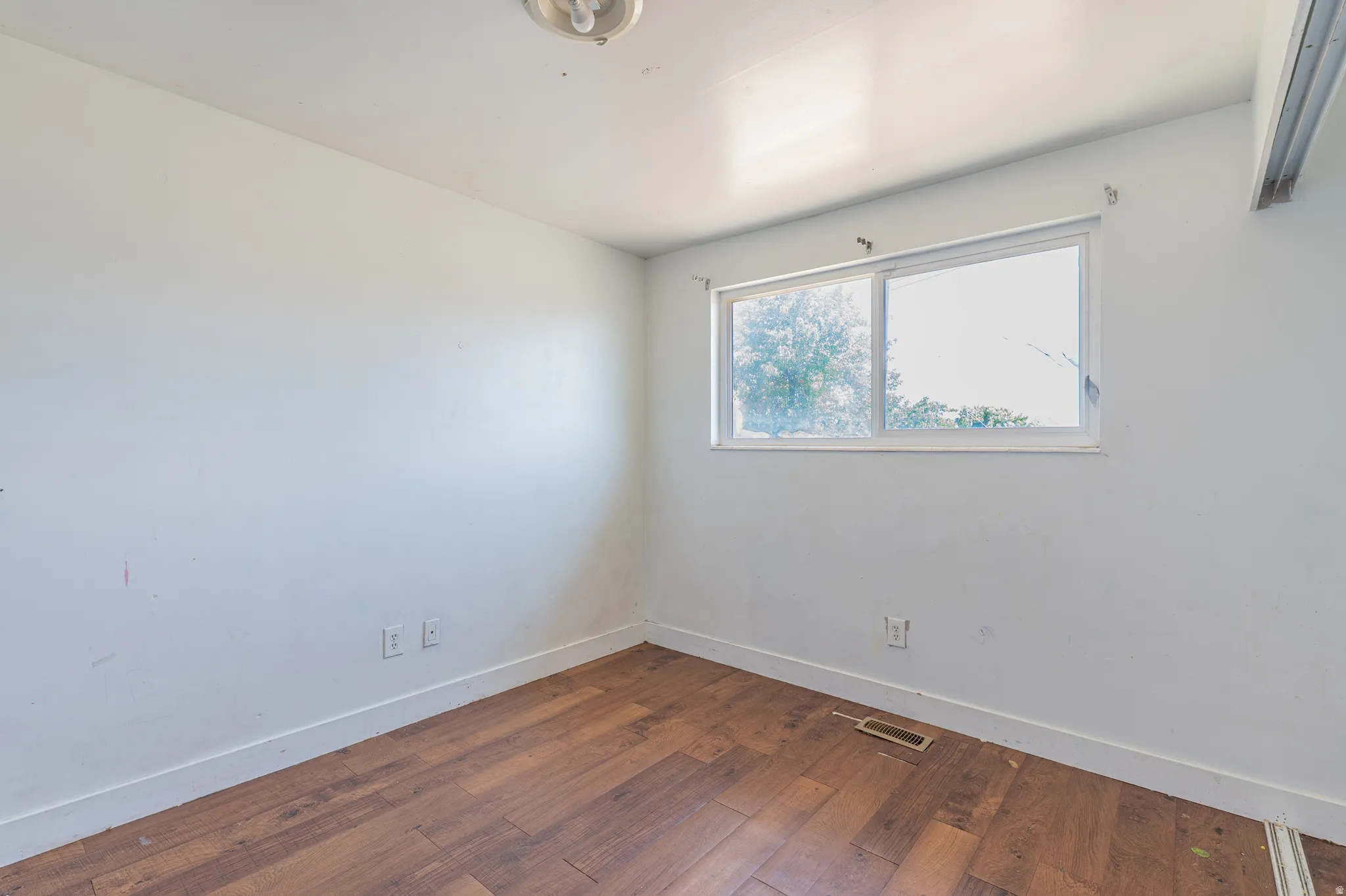 Bright room with wood-finish flooring, white walls, and a large window