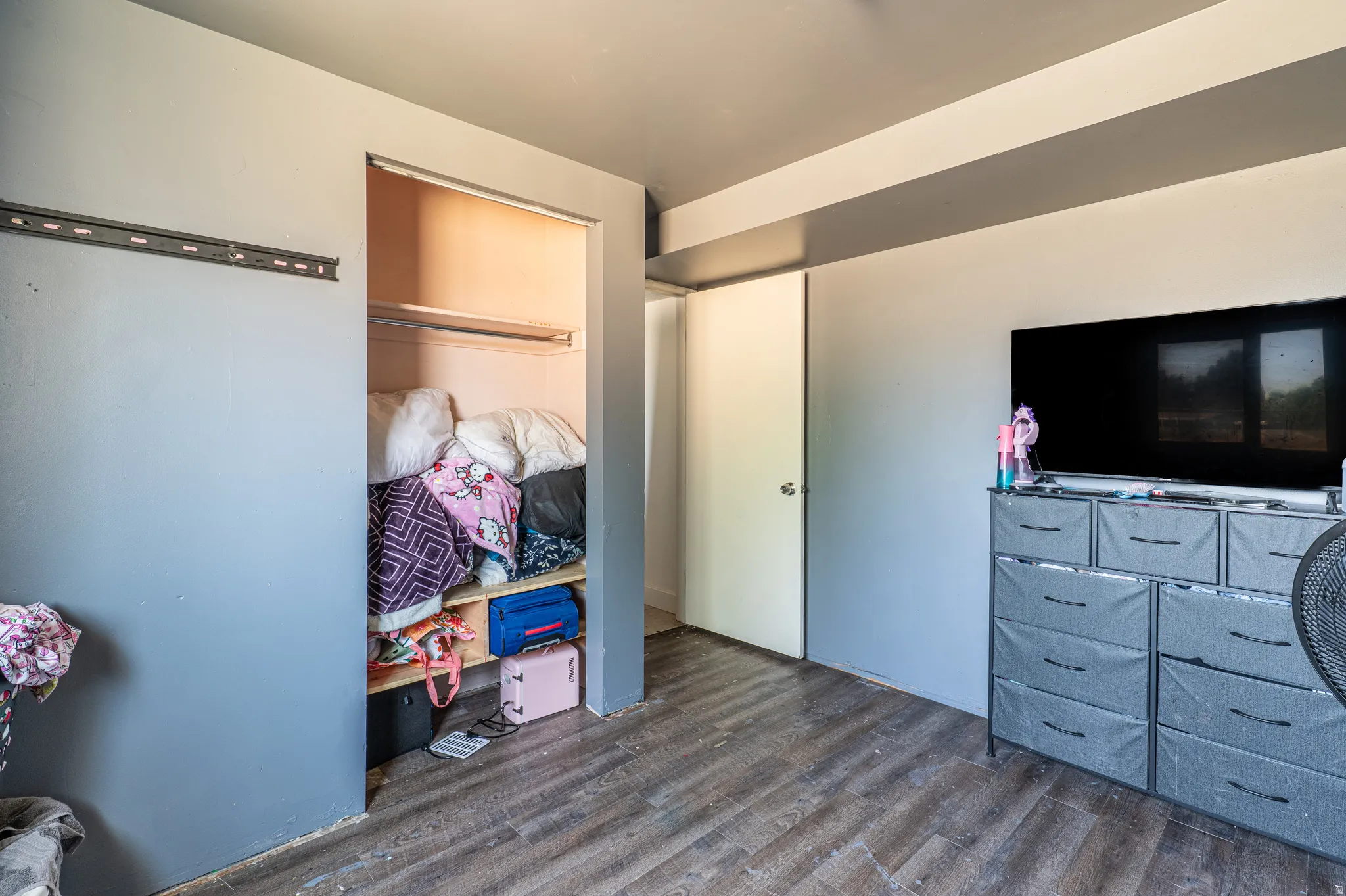 Room featuring wood-finish flooring, a built-in closet with shelving and hanging rod, and a neutral wall color