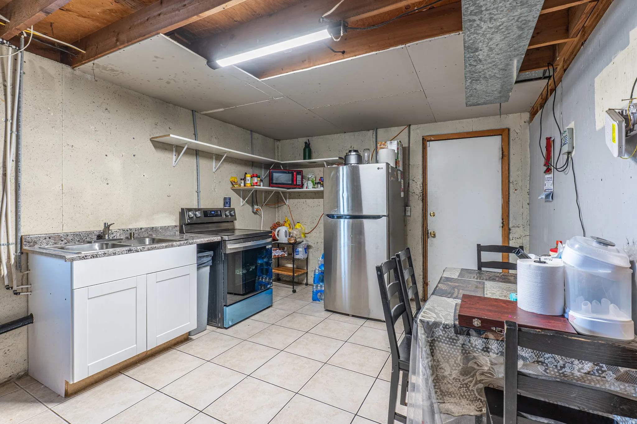 Basement kitchenette featuring white cabinetry, a double basin sink, and tiled flooring