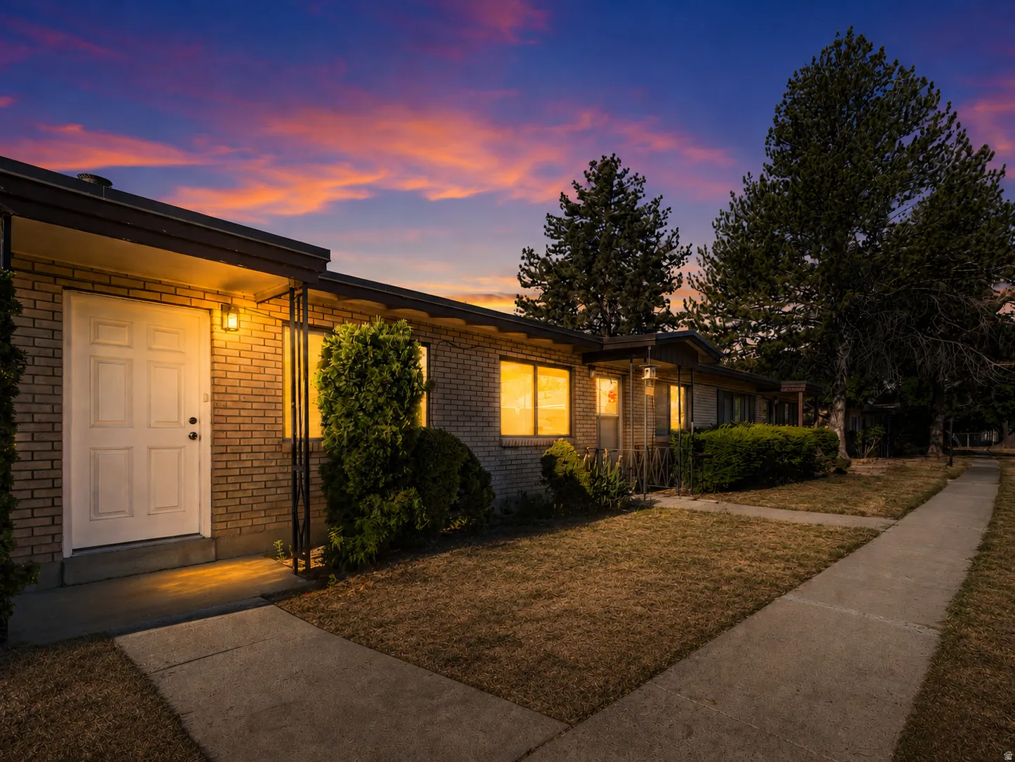 Brick facade residence with a covered entryway, exterior lighting, and established landscaping