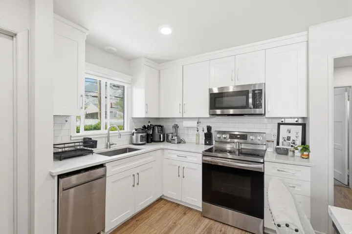 Kitchen featuring white shaker cabinetry, stainless steel appliances, white subway tile backsplash, and wood-finish flooring
