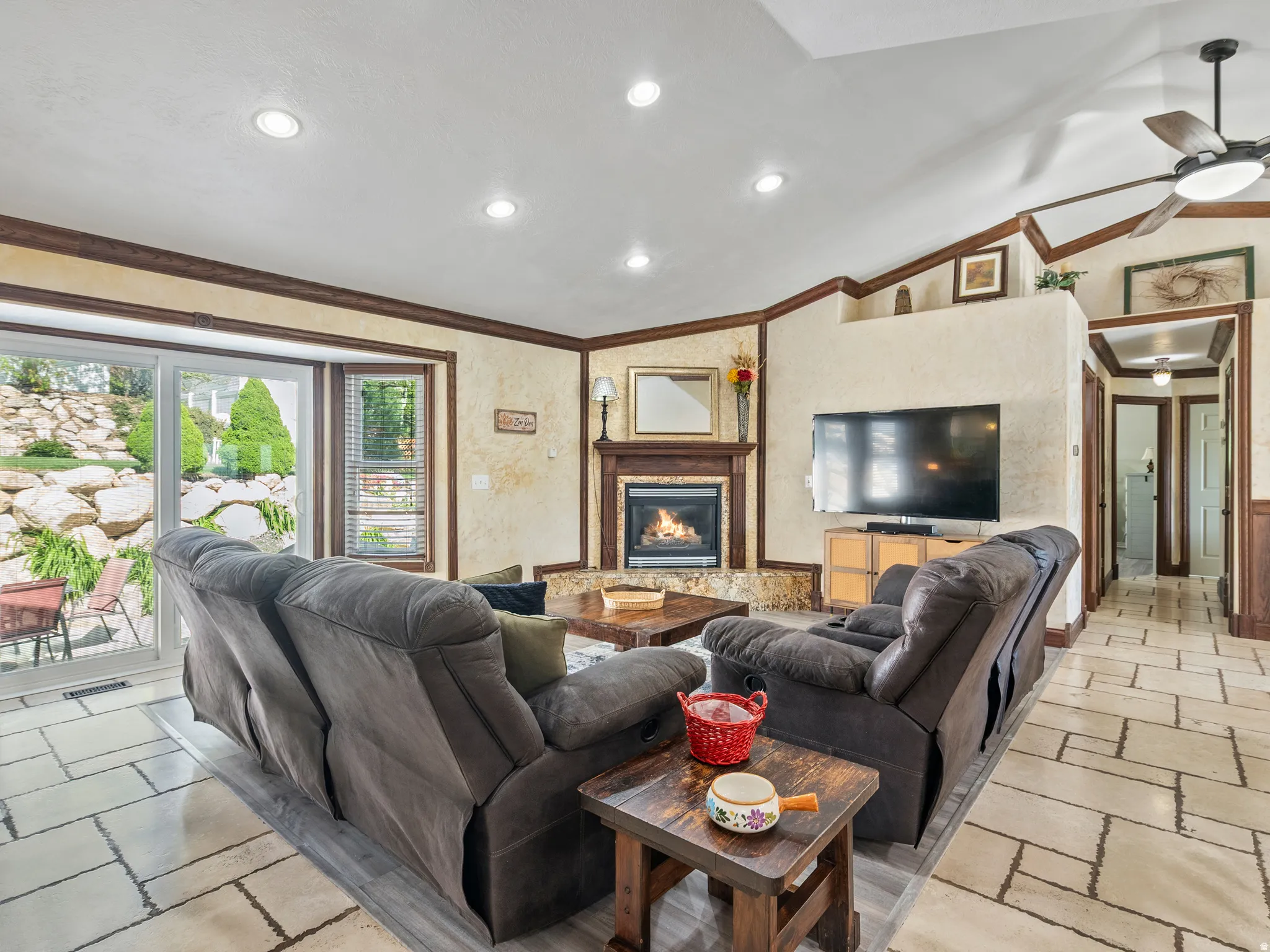 Spacious living area featuring a corner fireplace with stone surround, vaulted ceilings, recessed lighting, and a ceiling fan