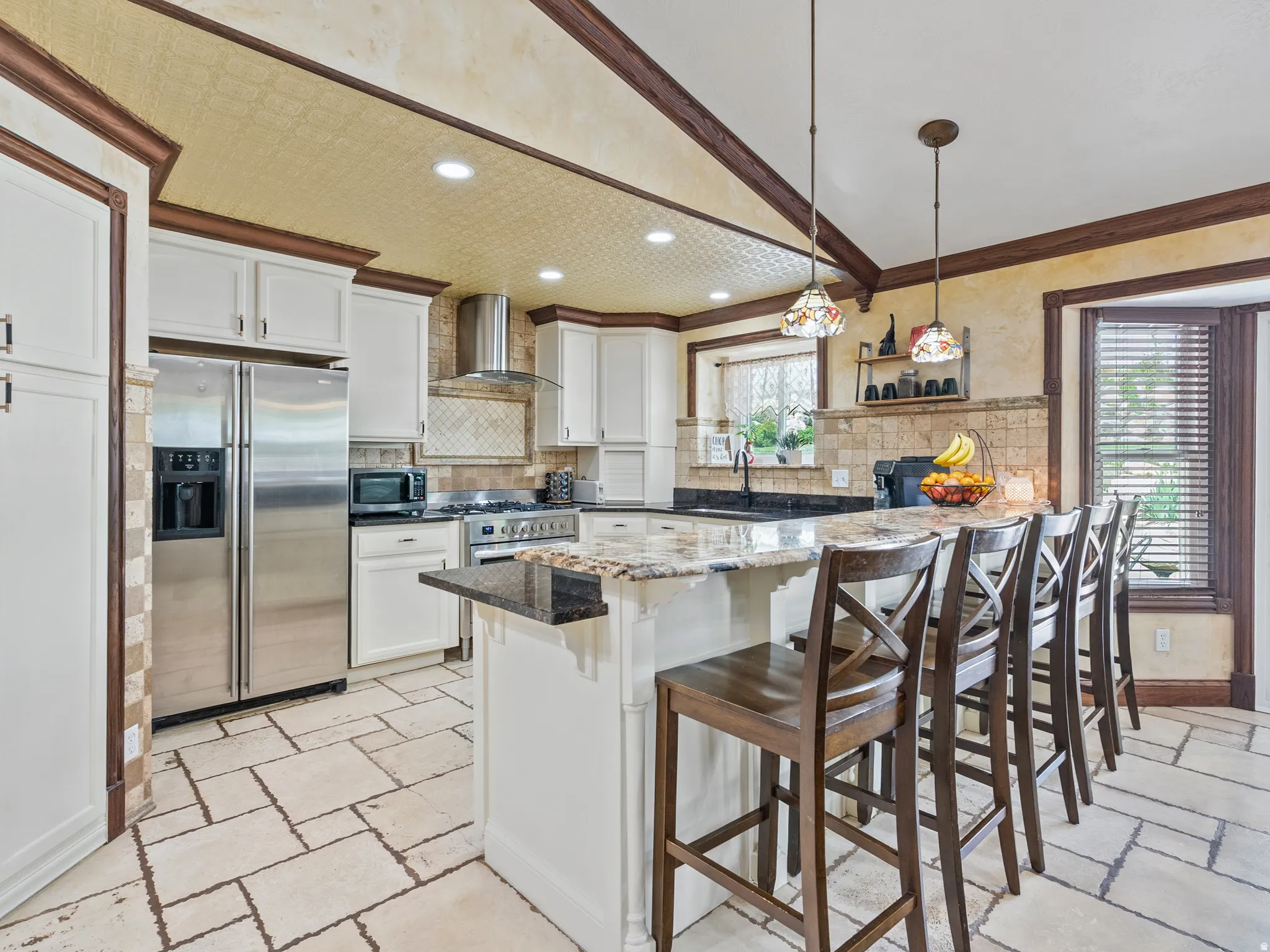 Kitchen featuring white cabinetry, stainless steel appliances, an island with seating, pendant lighting, and stone flooring