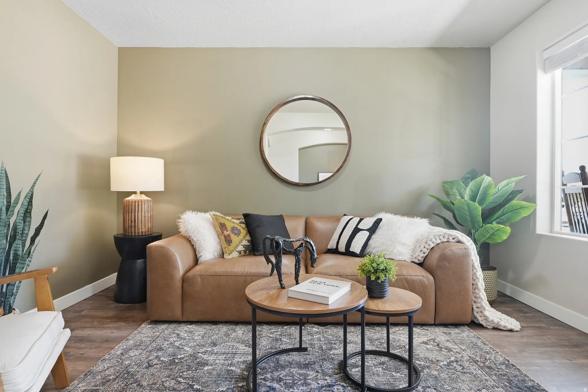 Spacious room featuring wood-finish flooring, a contemporary accent wall, a large window, a built-in wall mirror, and modern baseboards