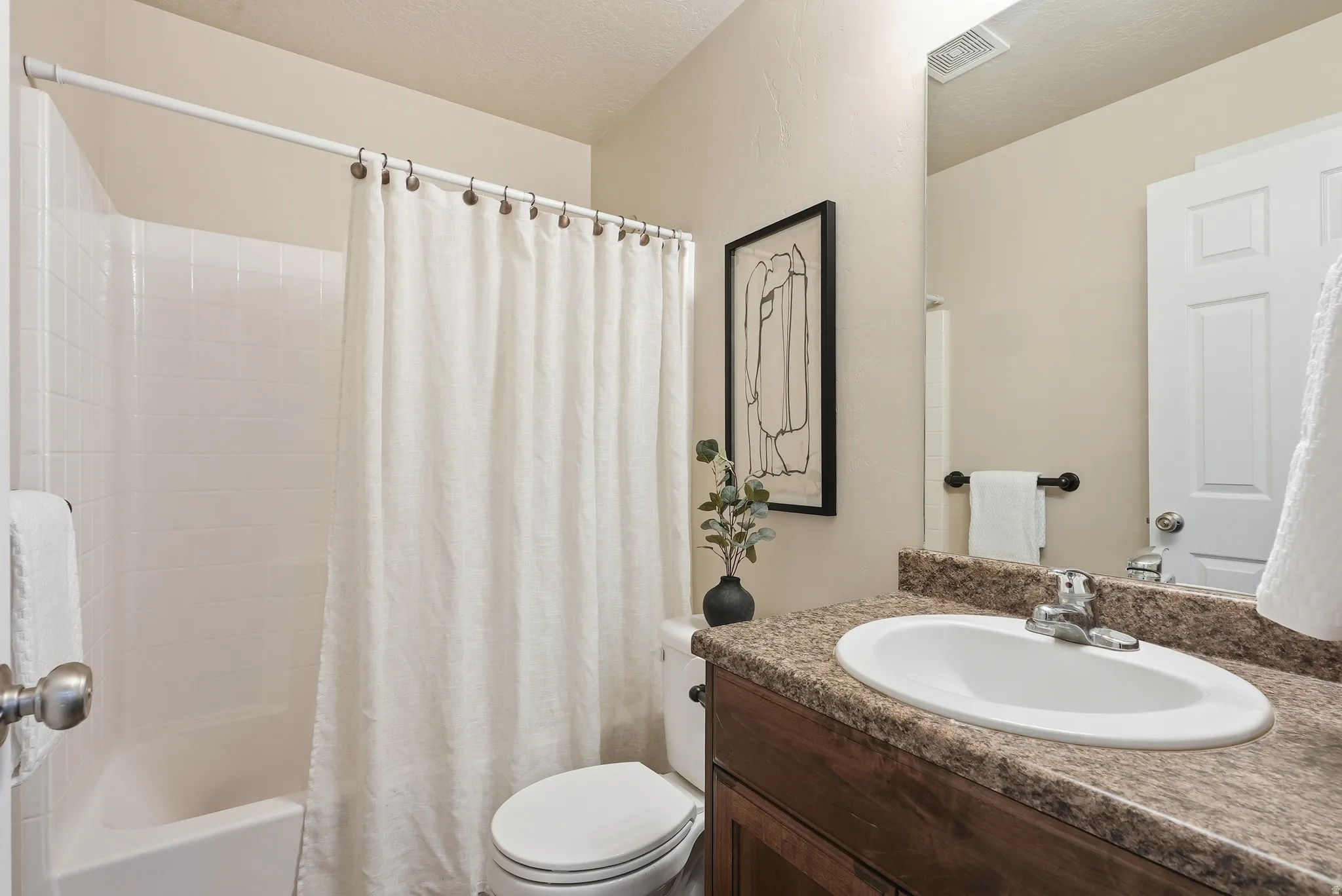 Bathroom featuring a built-in tub with tile surround, a dark wood-finish vanity with an integrated sink, and a speckled countertop