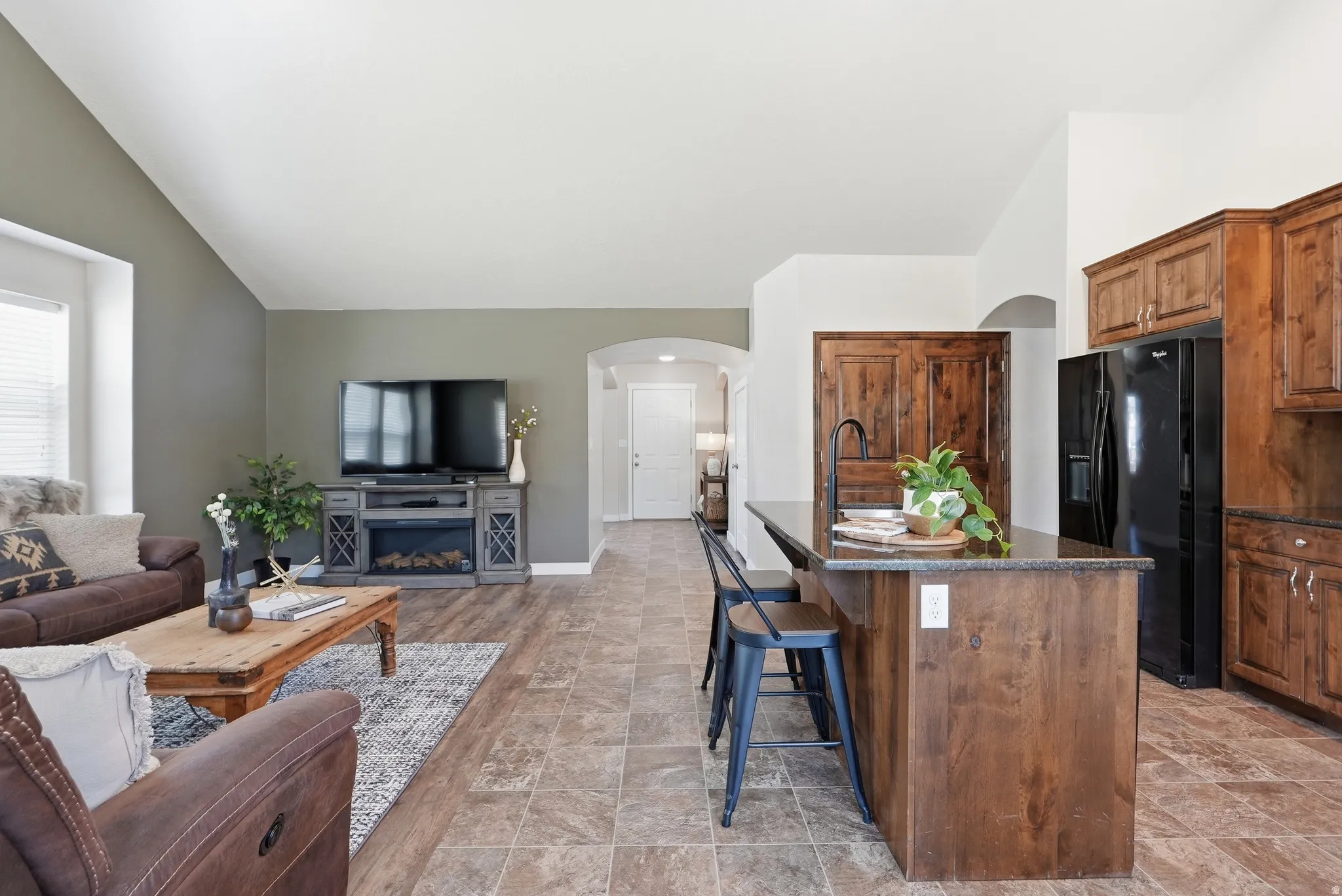 Open-concept living area featuring a vaulted ceiling, pantry and a kitchen island with seating