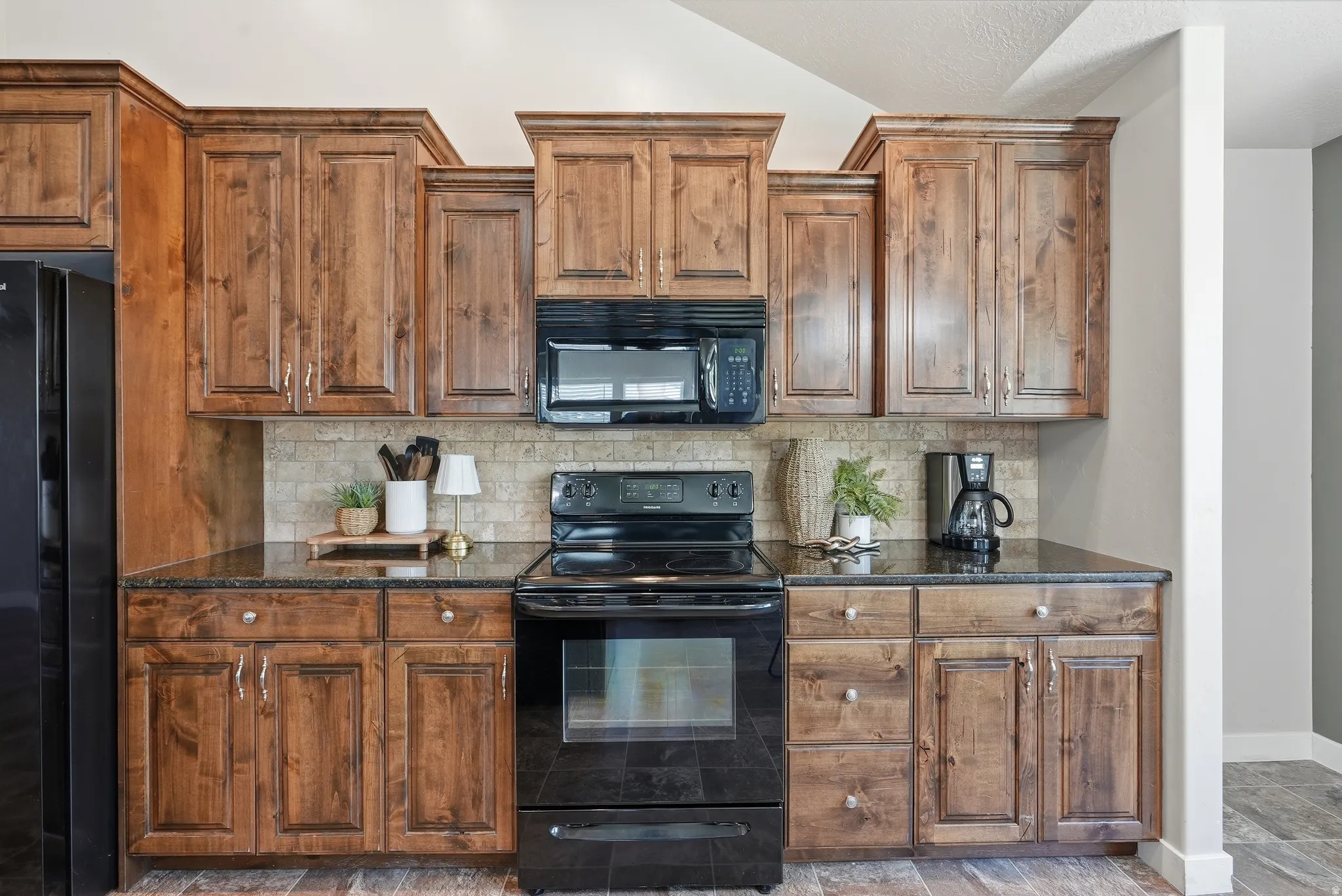 Kitchen featuring wood cabinetry, black appliances, a tile backsplash, and dark countertops