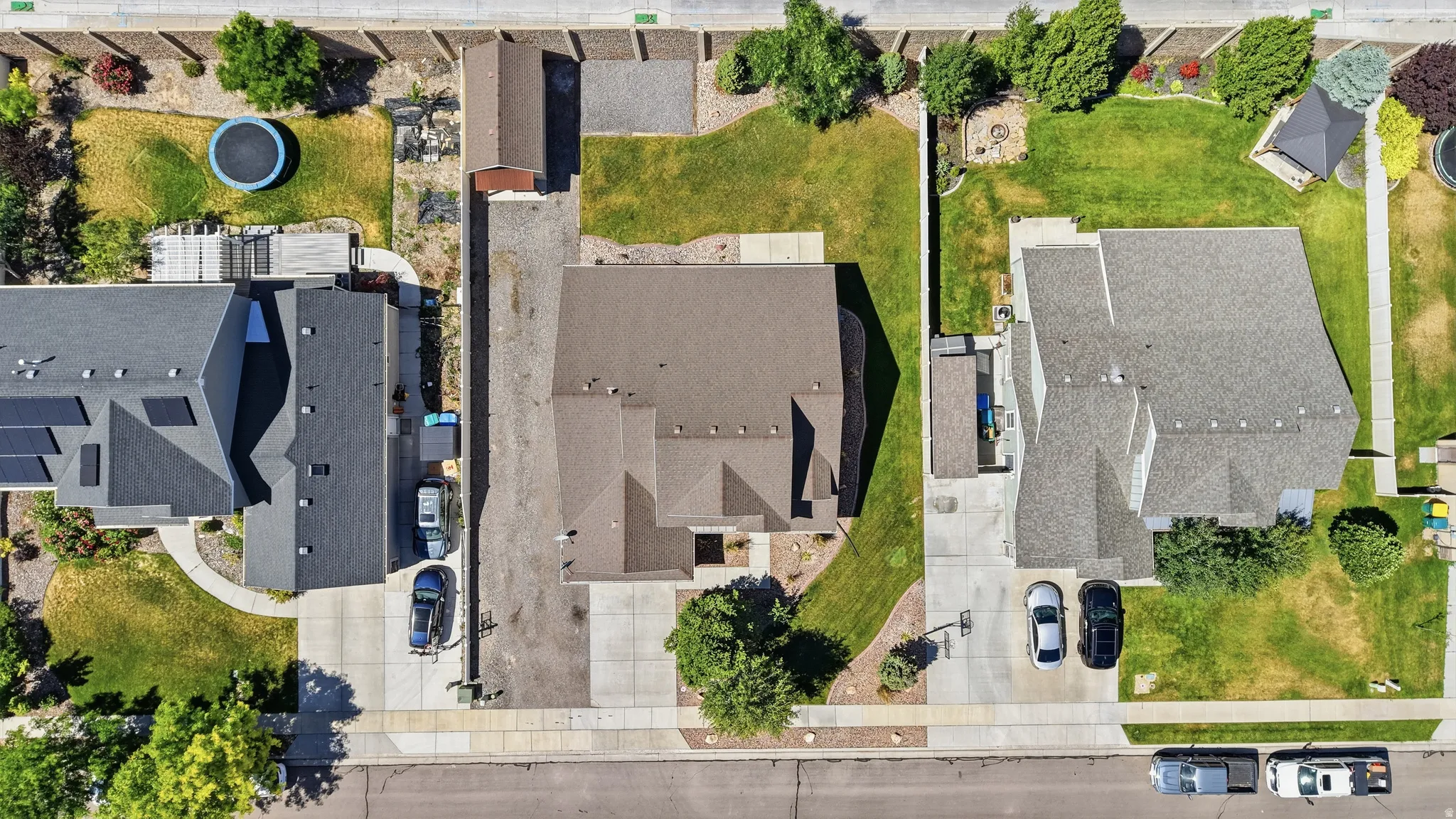 Property featuring a pitched roof, front yard with mature landscaping, a concrete driveway, and an adjacent side yard with an extended parking pad and detached garage
