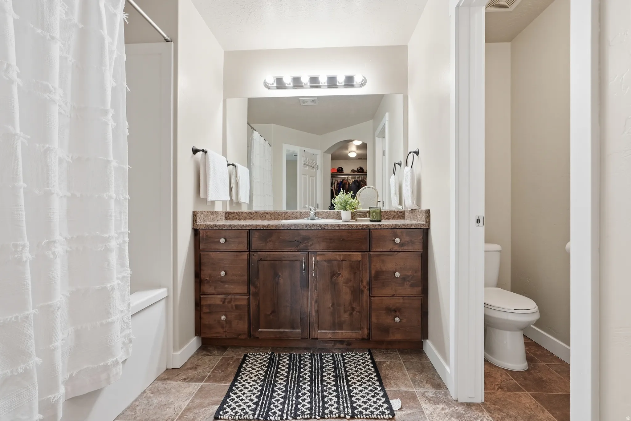 Primary en suite bathroom featuring a dark wood vanity with a light-colored countertop, an undermount sink, and a large mirror