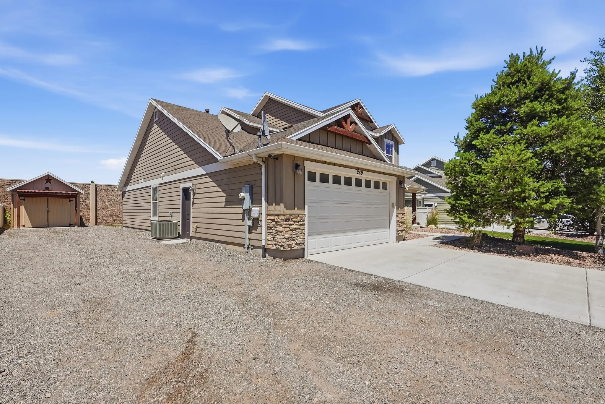 Two-story residential exterior featuring a light brown siding, stone accents, and a front-facing garage with a concrete driveway, RV parking and detached garage