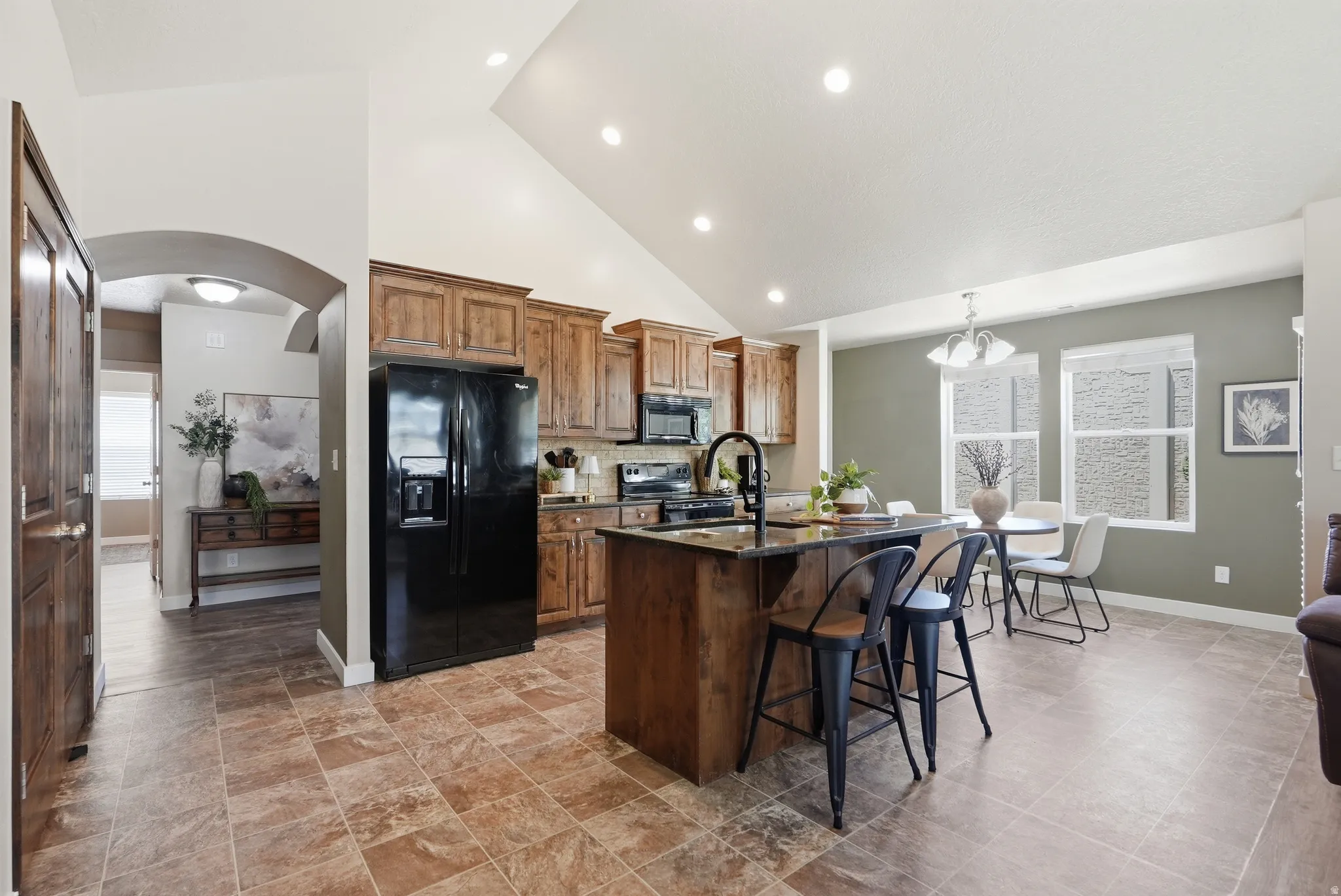 Spacious kitchen featuring wood cabinetry, black appliances, a central island with bar seating, and recessed lighting