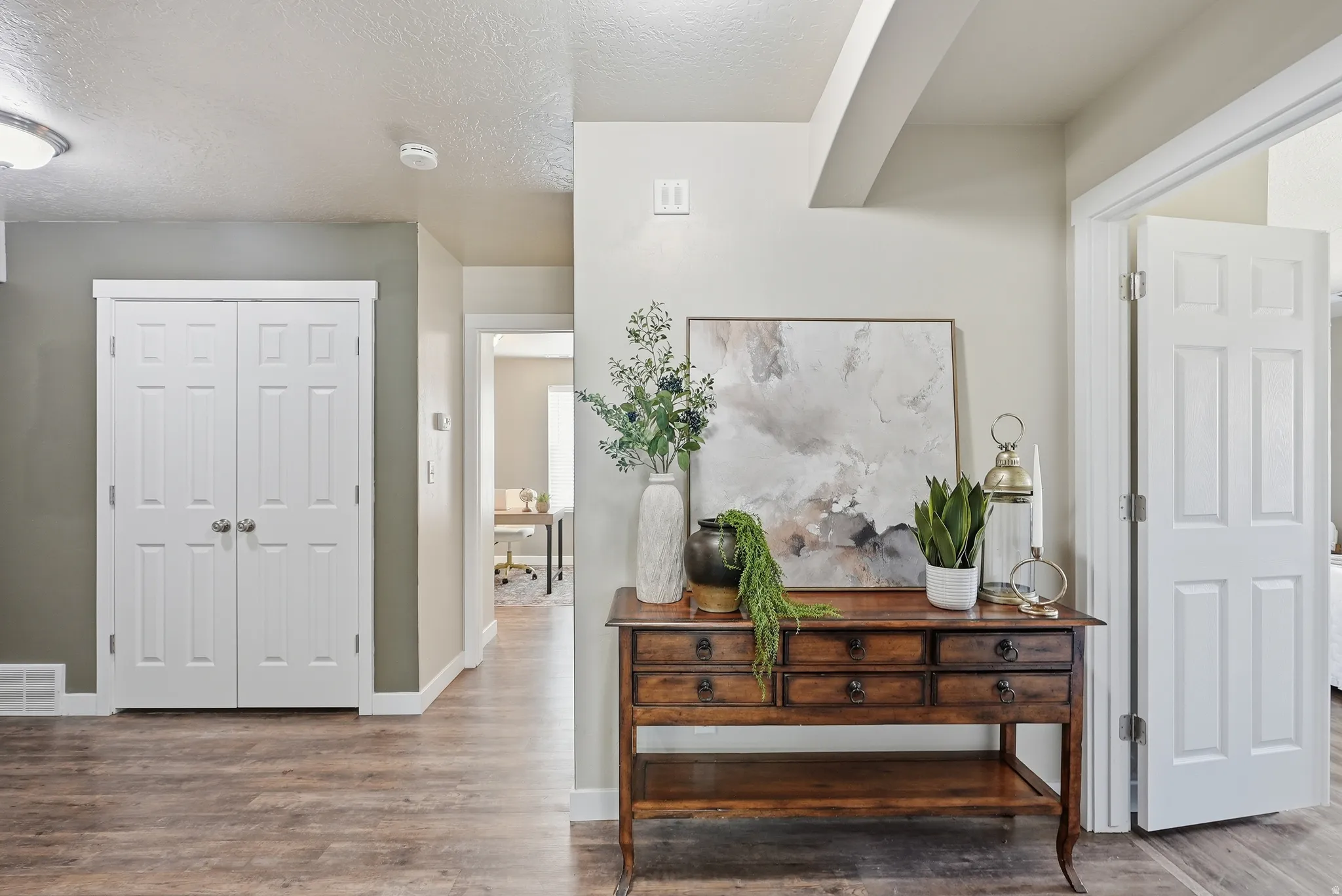 Main hallway featuring wood-finish flooring, light neutral paint, white trim, and a six-panel door to the main floor laundry