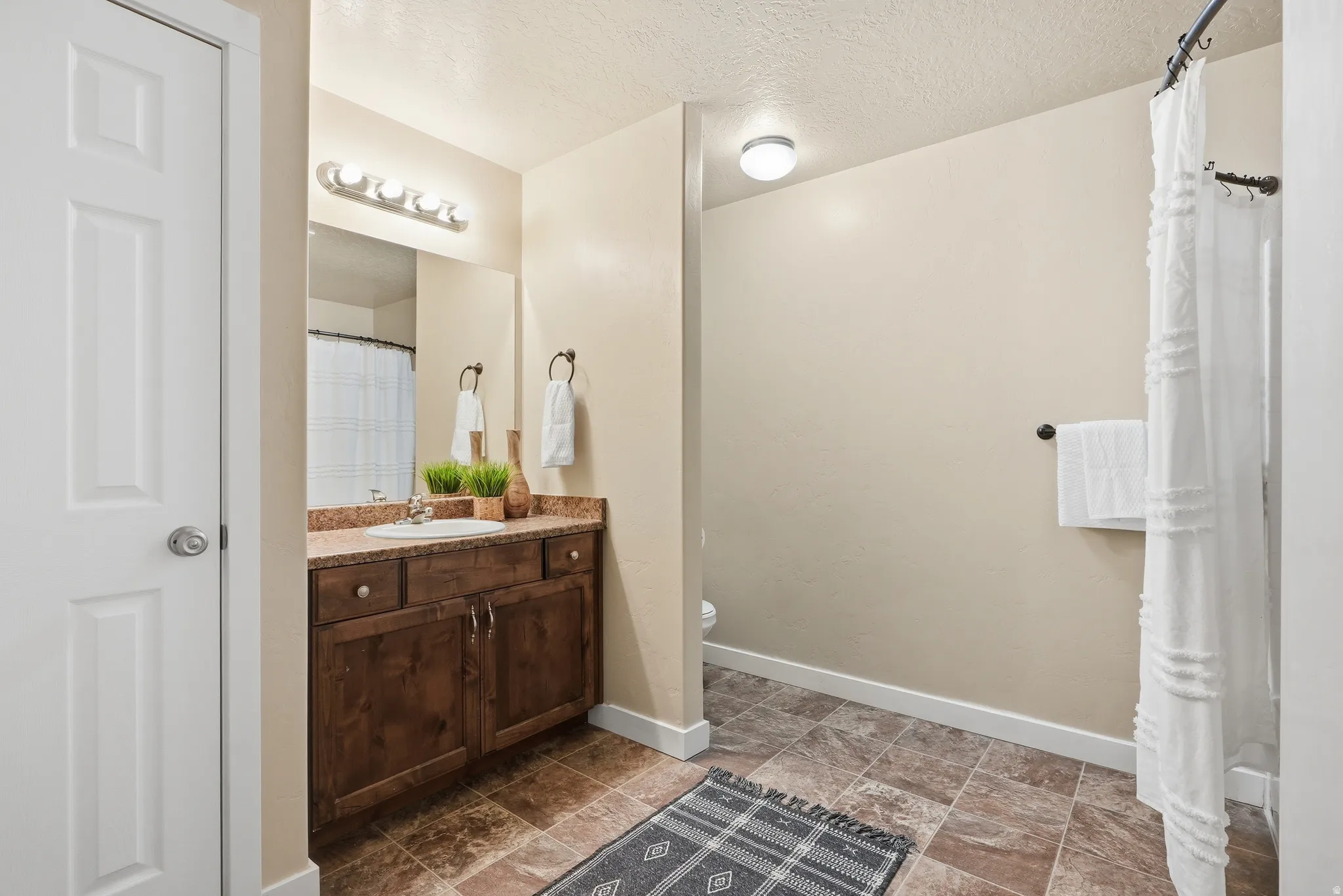 Large bathroom featuring a dark wood-finish vanity, light-toned countertop with an integrated sink, rectangular mirror, and a wall-mounted light fixture