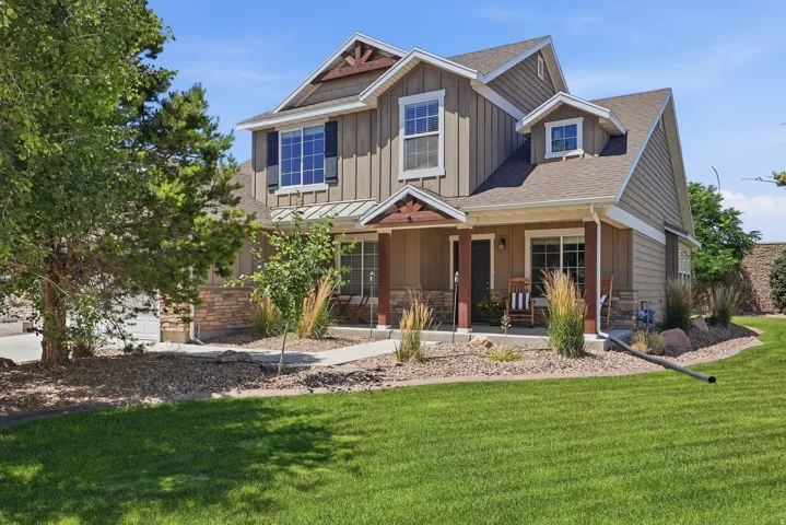Contemporary two-story residence featuring a covered front porch, mixed siding and stone veneer, dormer windows, and an attached garage with a paved driveway