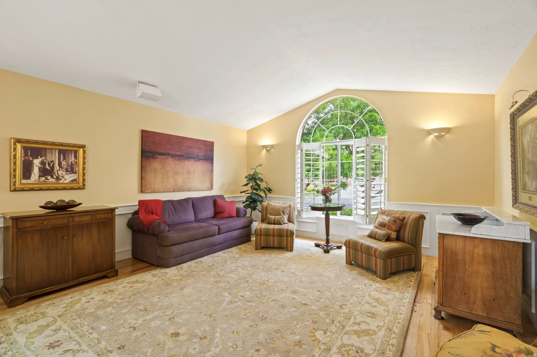 Living area featuring an arched window with wood shutters, hardwood flooring, and wainscoting