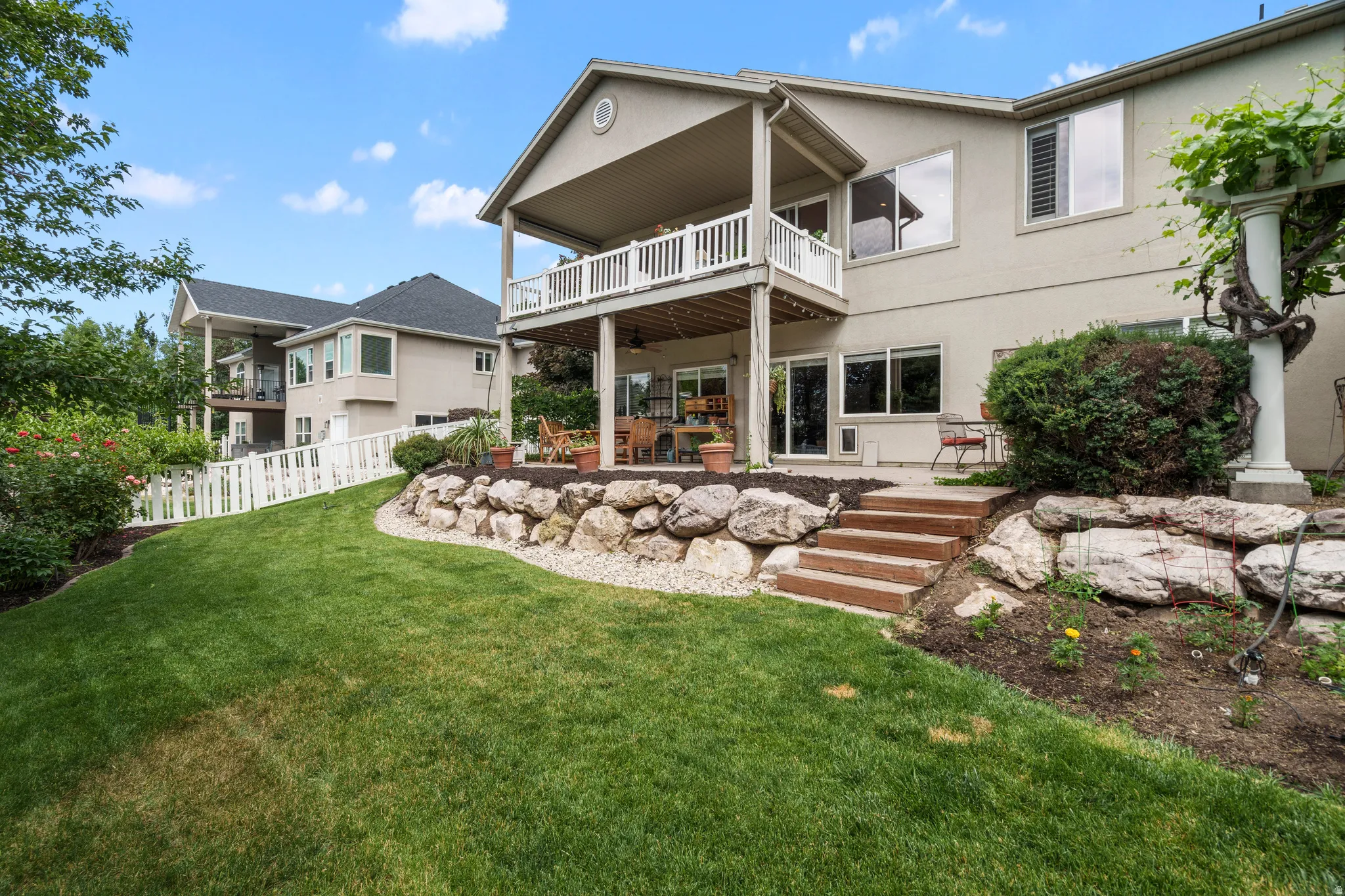 Tiered backyard featuring a covered upper-level deck, a lower patio space, and a manicured lawn