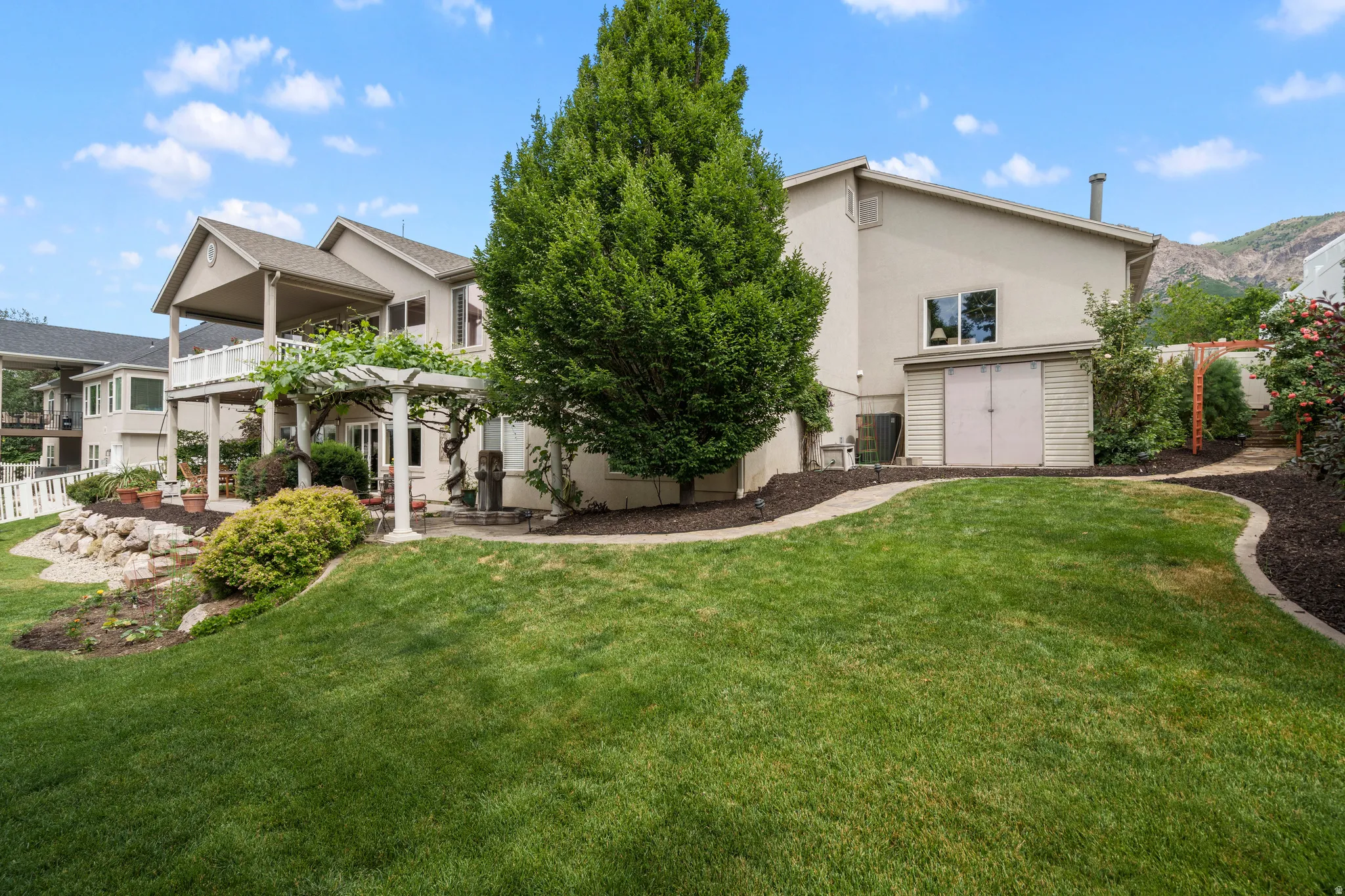 Expansive rear lawn with established landscaping, a multi-level deck, and a detached storage shed