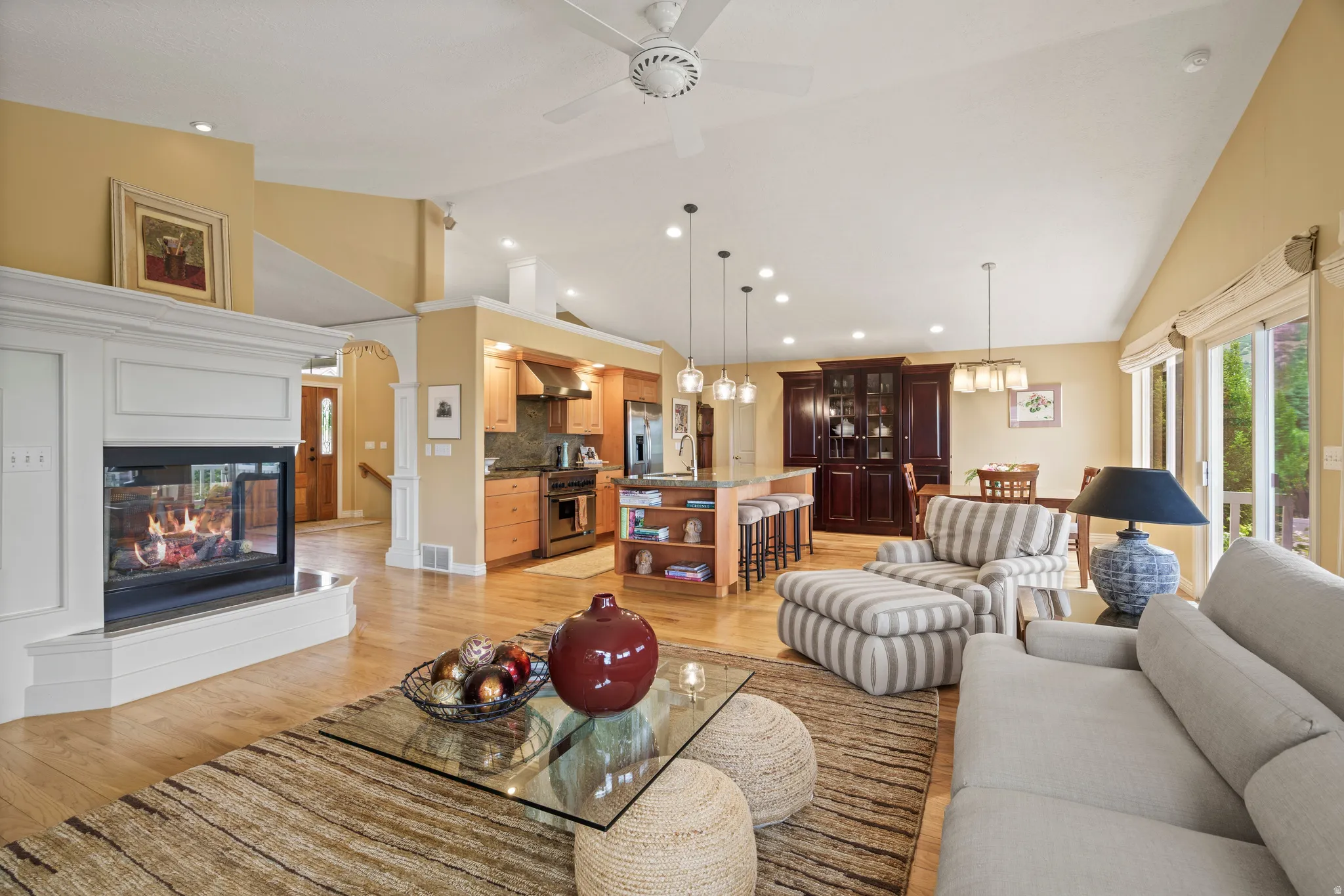 Open-concept living space featuring vaulted ceilings, wood-finish flooring, and a corner gas fireplace with a white mantel