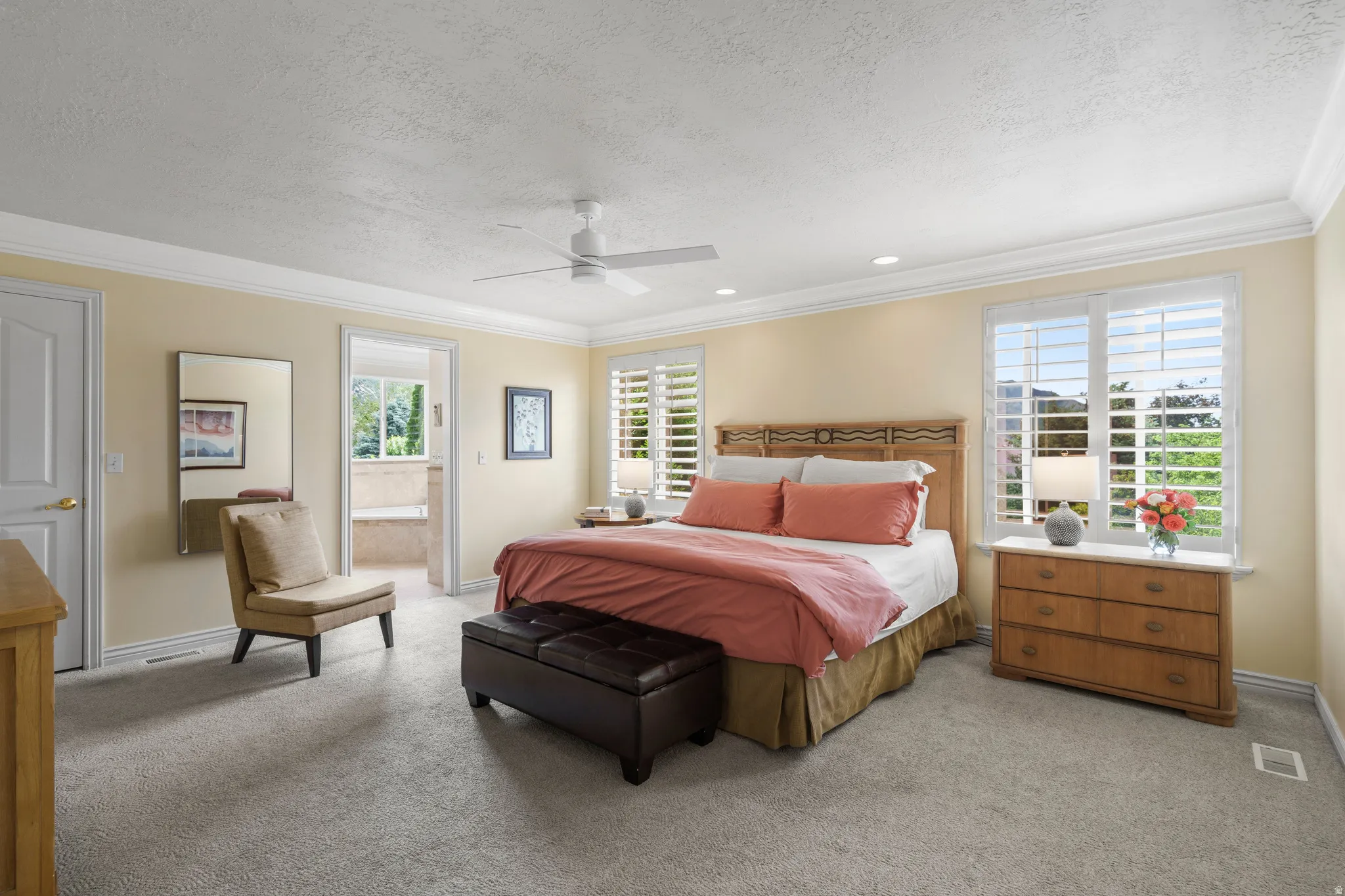 Spacious primary bedroom featuring  wood shutters, windows  with mountain, crown molding, and recessed lighting